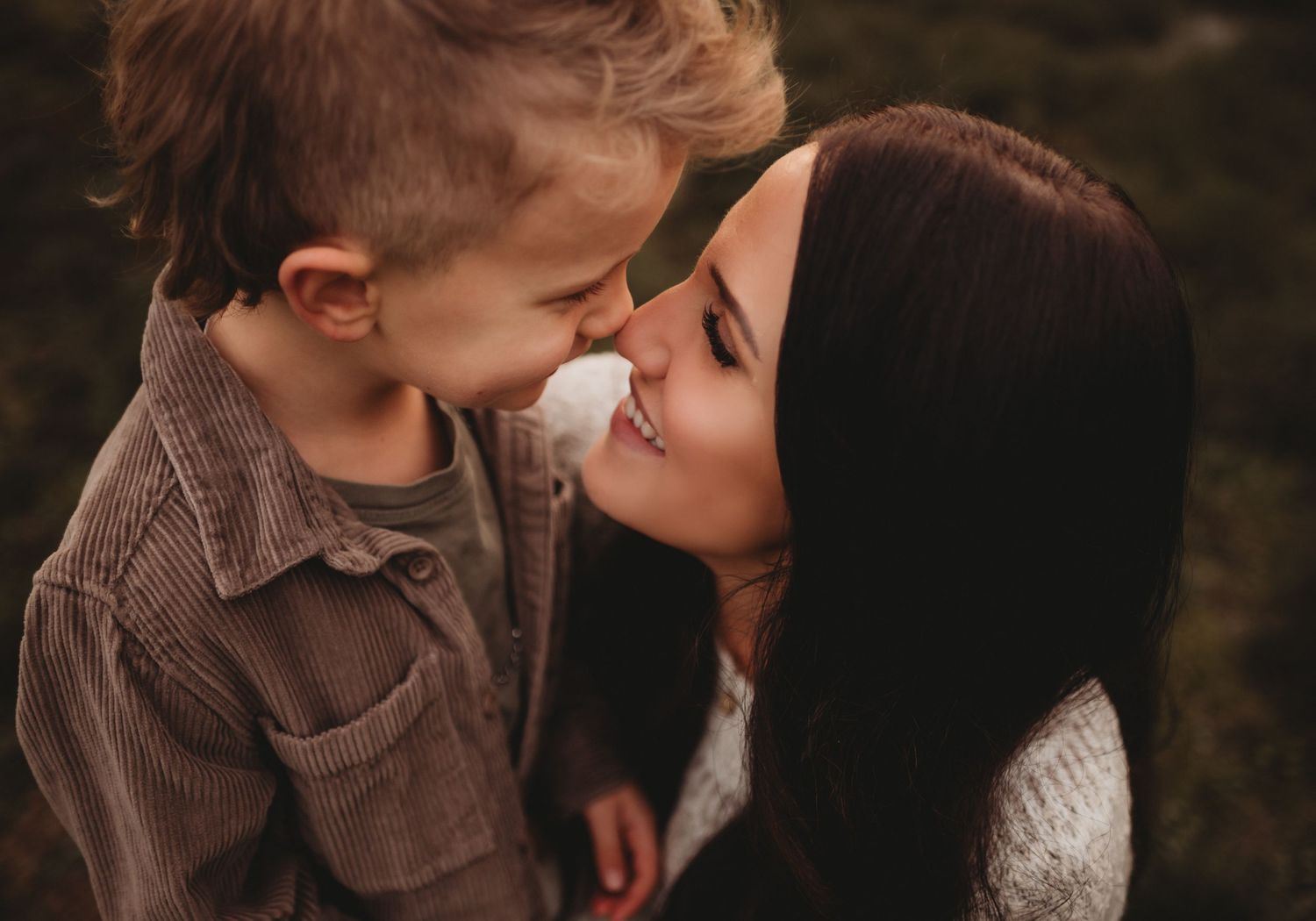Tender moment between a dark-haired mother and young child touching noses and smiling.