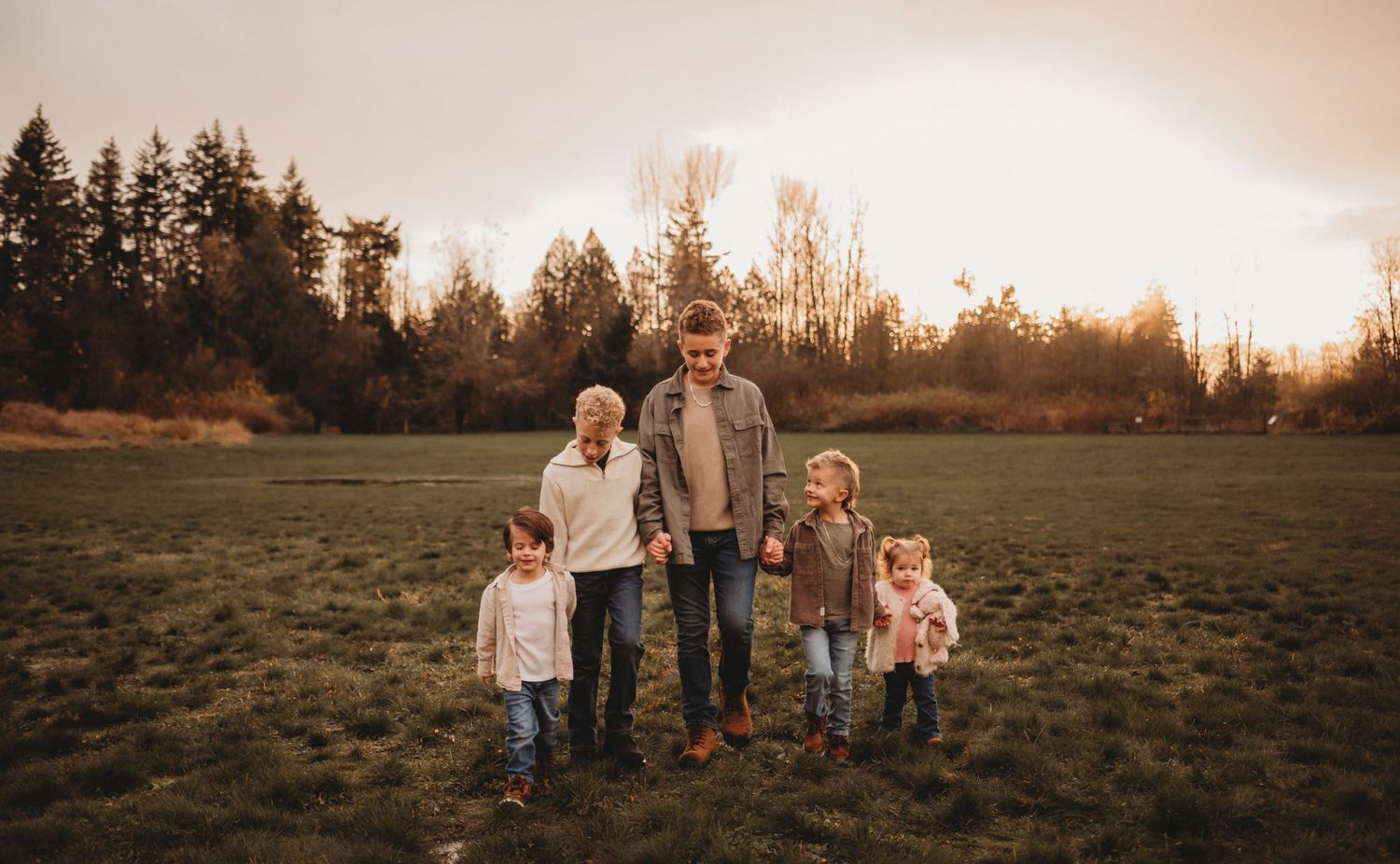 A happy family of five walks together in a green field during a warm sunset outdoor session.