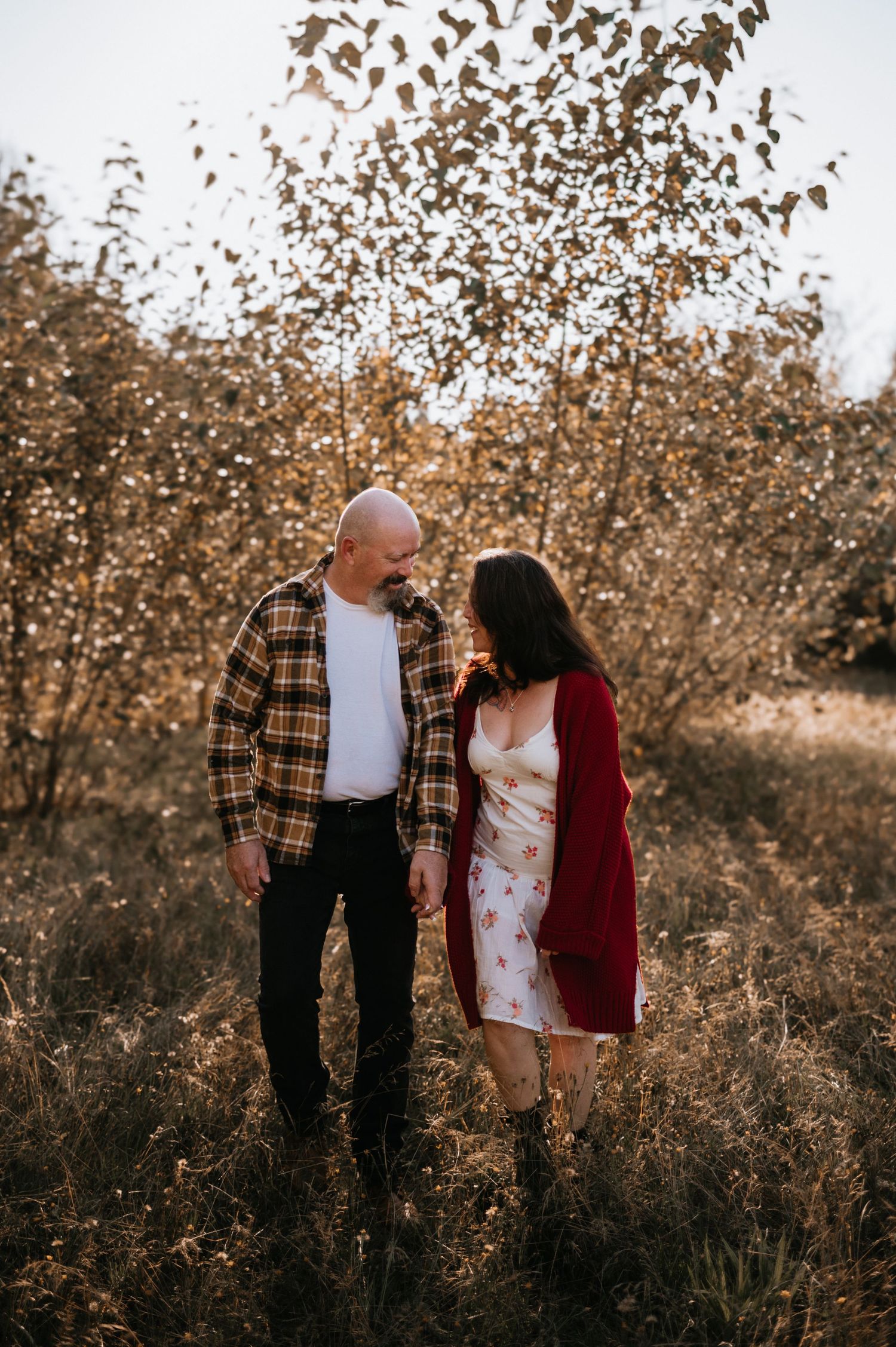 Couple walking hand in hand through autumn foliage with golden leaves falling around them.