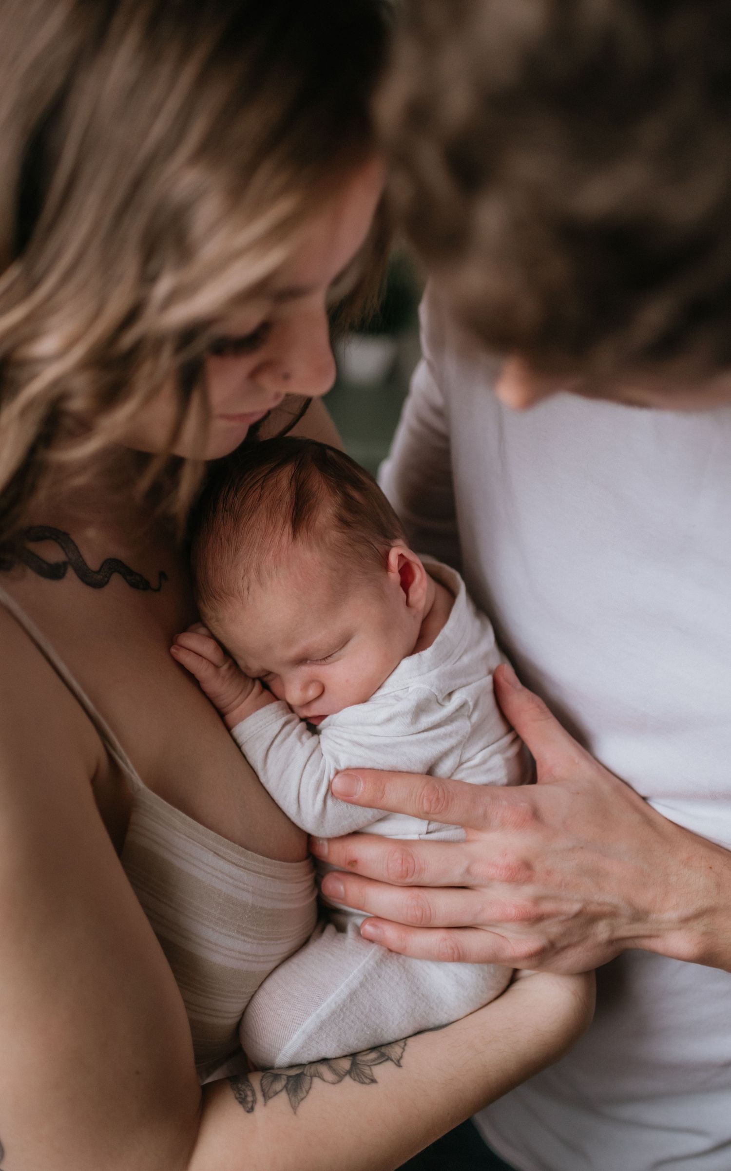 Close-up of tattooed mother and father lovingly gazing at sleeping swaddled newborn baby.