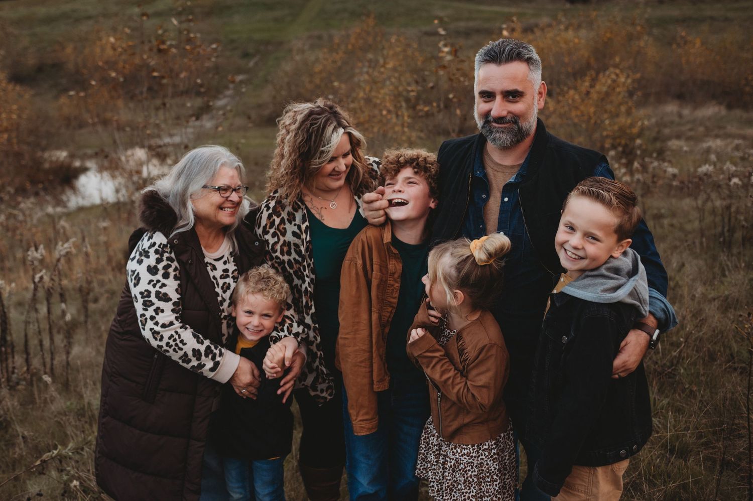 A happy multigenerational family smiles and laughs together in a golden autumn outdoor setting.