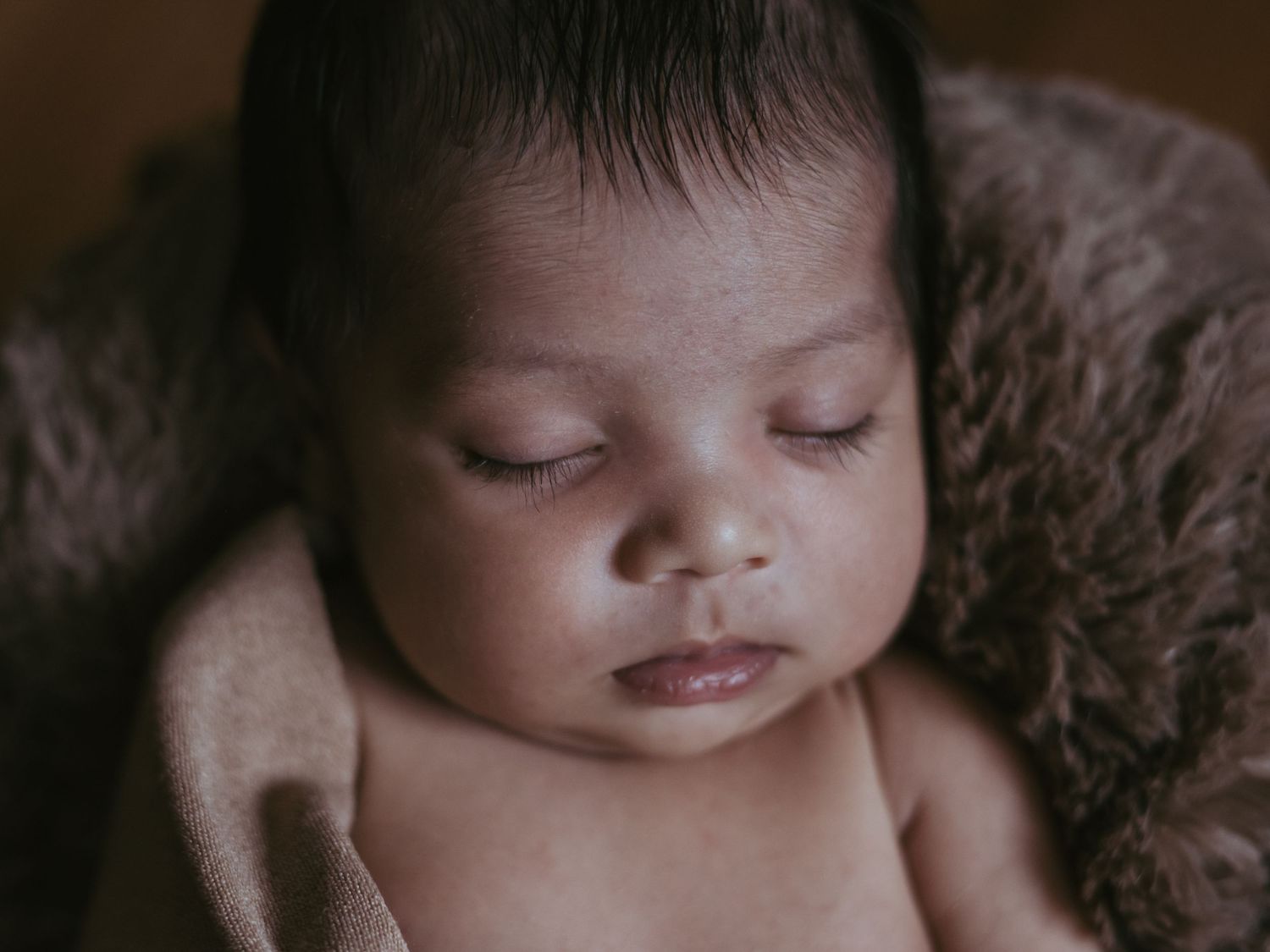 Close-up portrait of a peaceful sleeping newborn baby wrapped in a soft brown blanket.