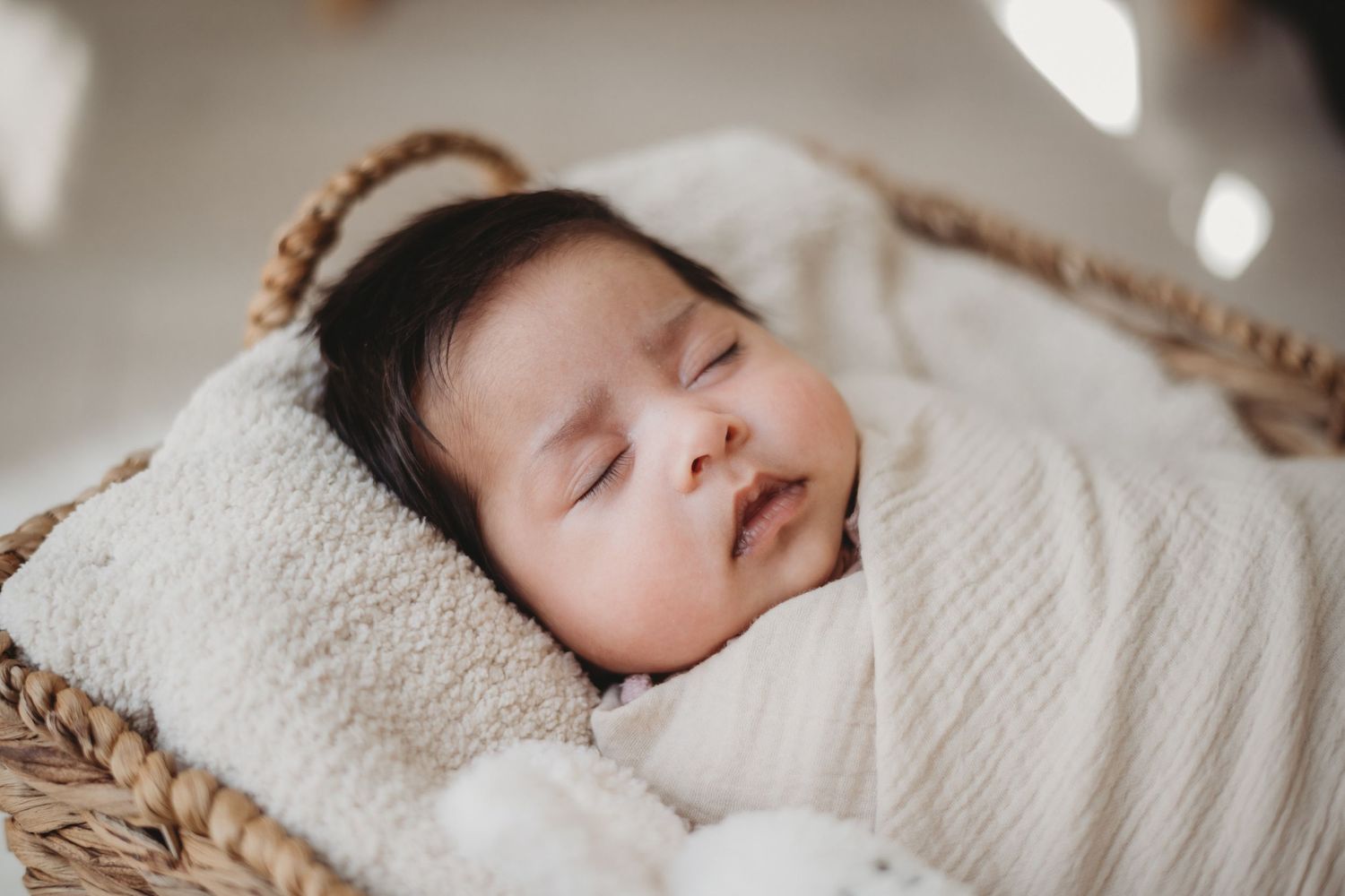 Serene newborn baby sleeping peacefully swaddled in white wrap inside wicker basket.
