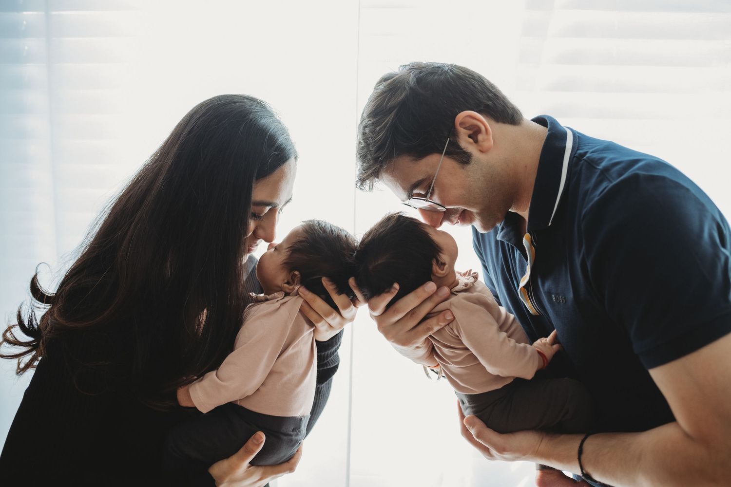 Parents gently touching foreheads with their two newborn twins in a tender and loving moment.