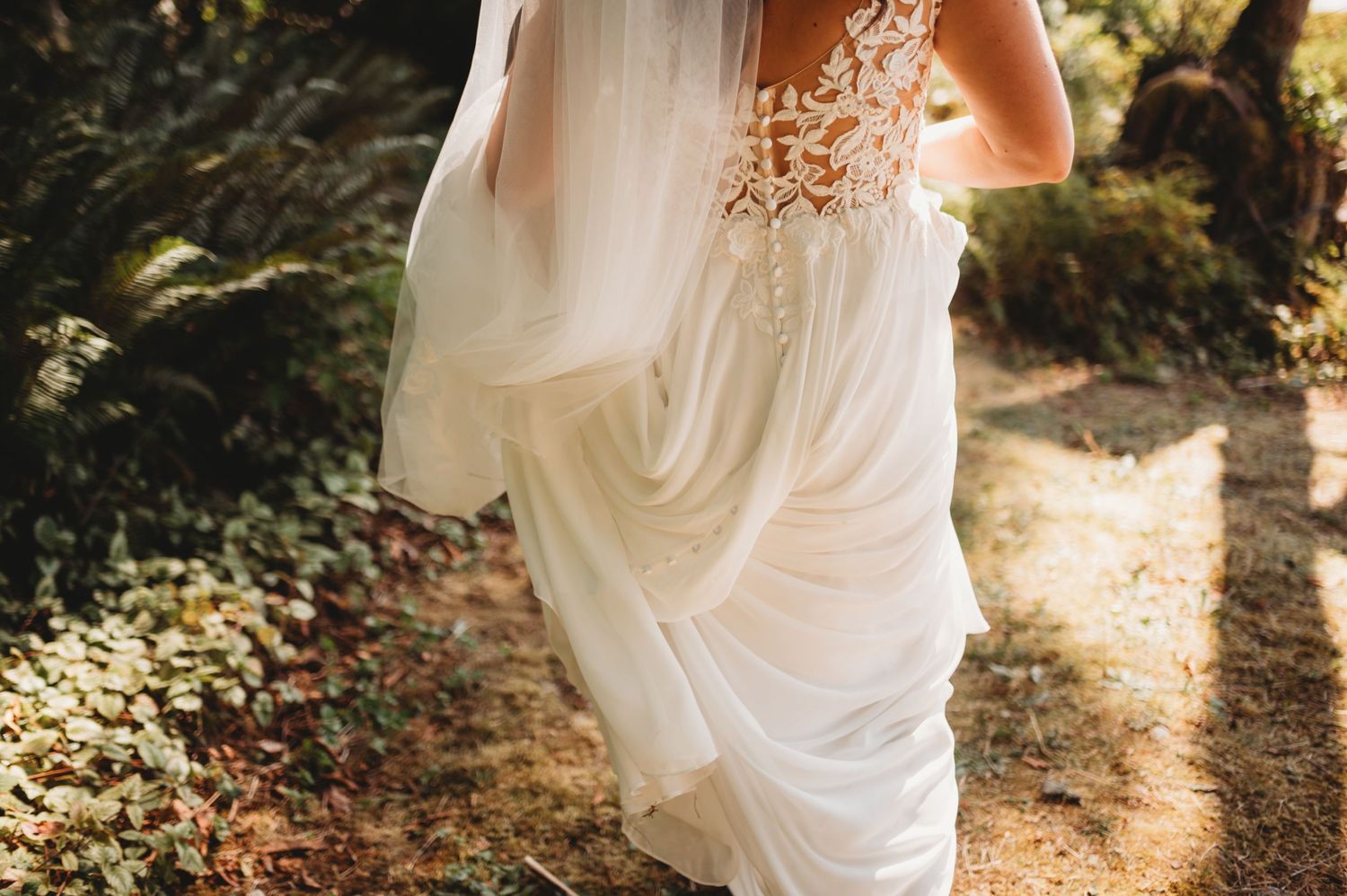 Close-up of bride in lace wedding dress with flowing veil in garden.
