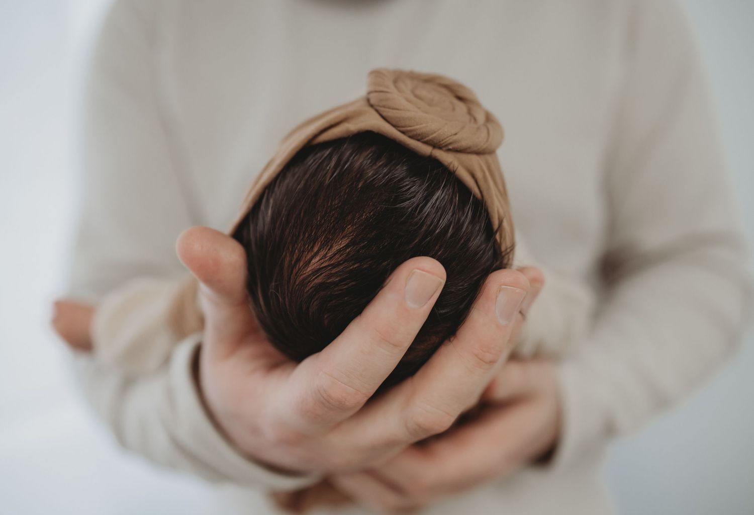 Father gently cradling a newborn baby's head in his hands during a newborn photo session.