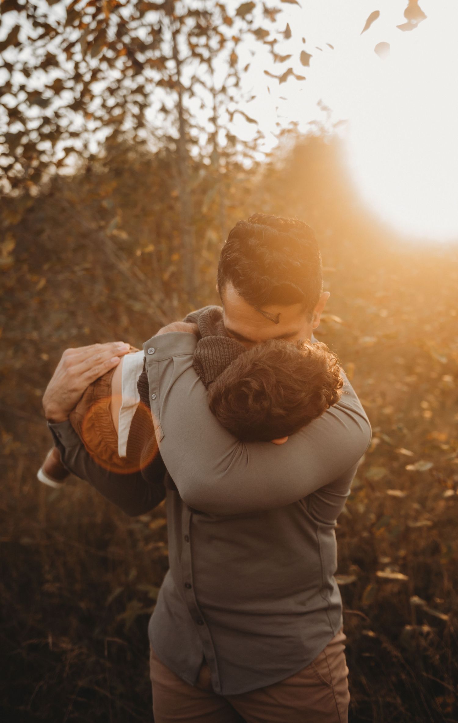 Parent embracing child in golden autumn sunlight outdoors.