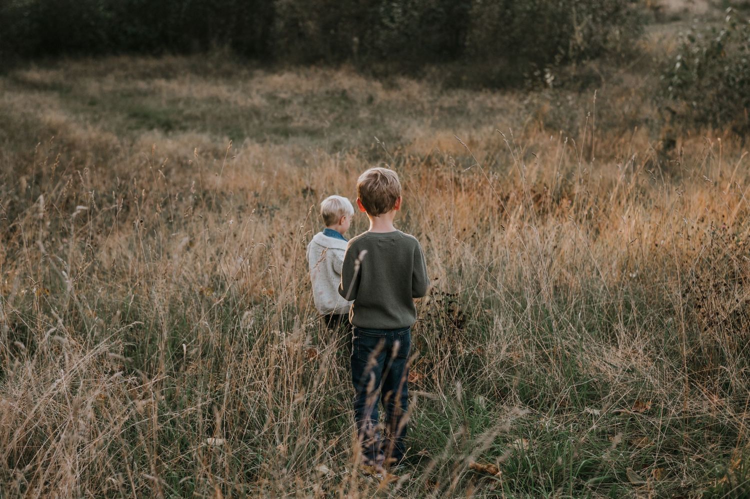 Two young children walking through tall golden grass field in autumn.