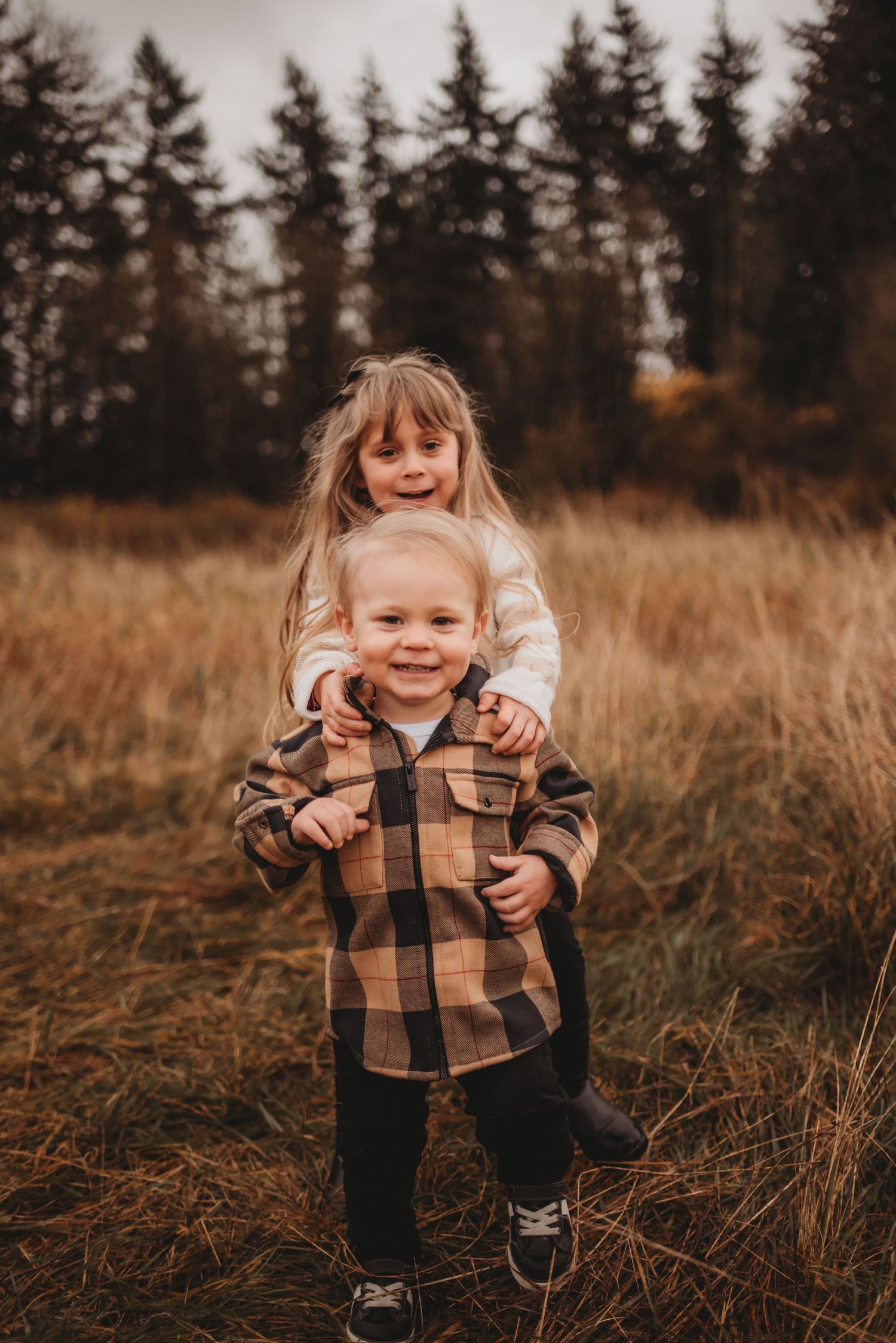 Young girl hugging toddler boy in plaid shirt in autumn field.