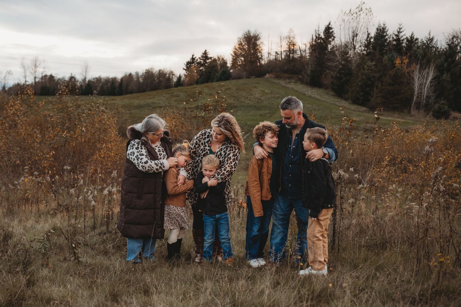 A multigenerational family gathers closely together laughing in a golden autumn meadow setting.