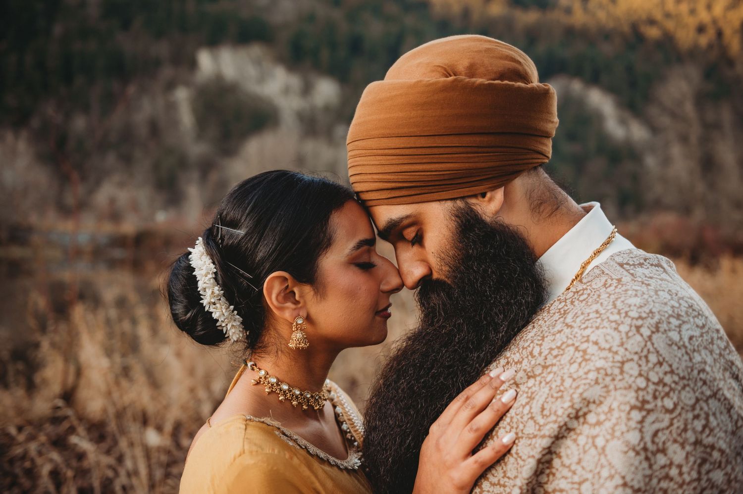 Sikh wedding couple sharing a romantic forehead touch, bride adorned with gold jewelry and floral hair accessories.