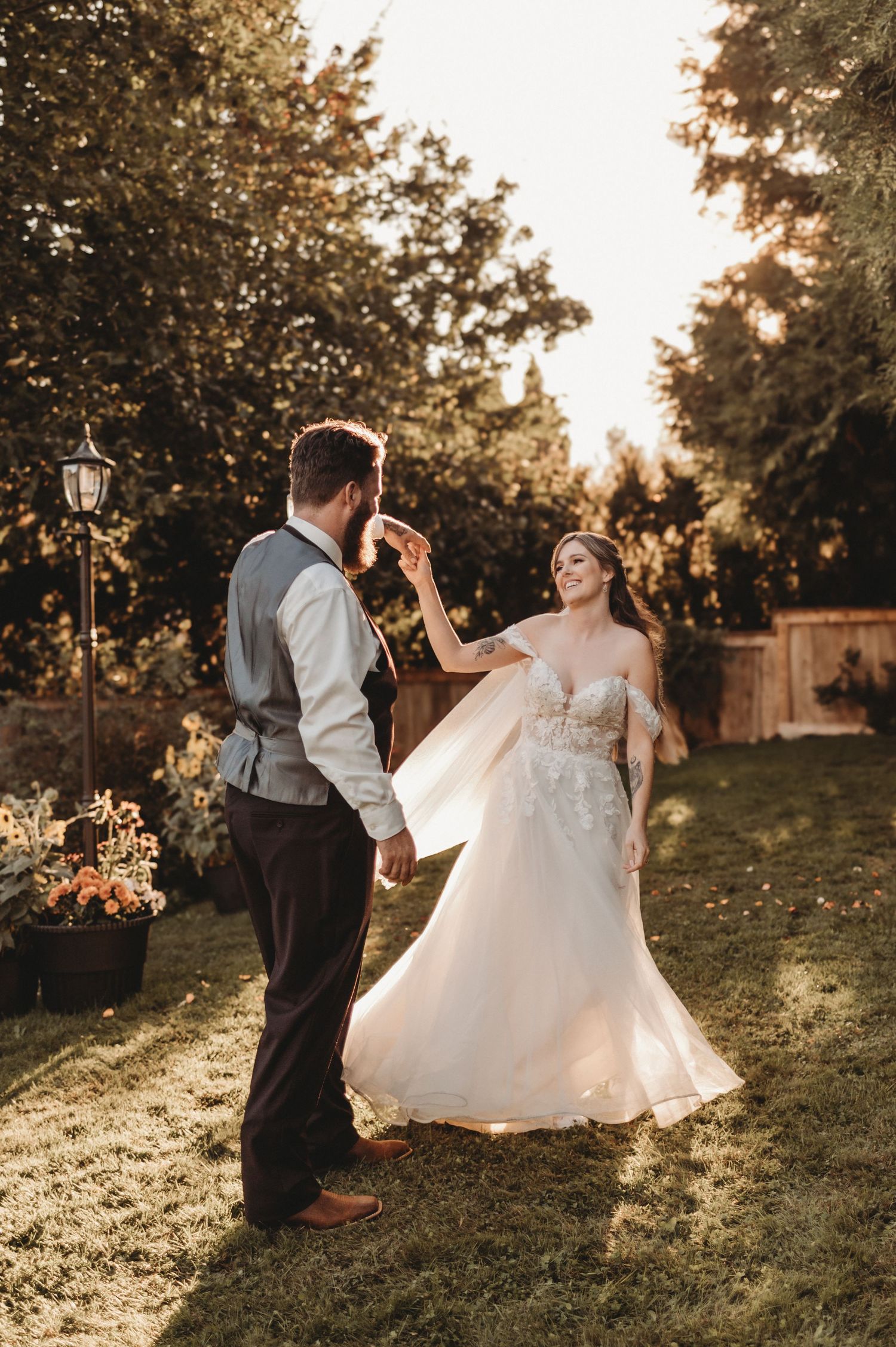 Bride and groom dancing together in golden sunset light in a lush garden, bride wearing a floral lace wedding gown.