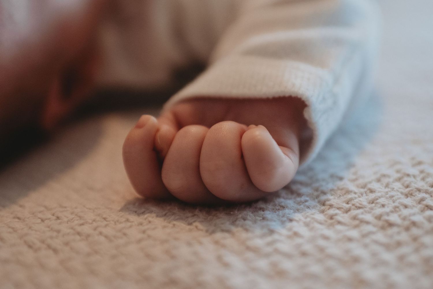 Close-up of a newborn baby tiny clenched fist resting on a textured white blanket.