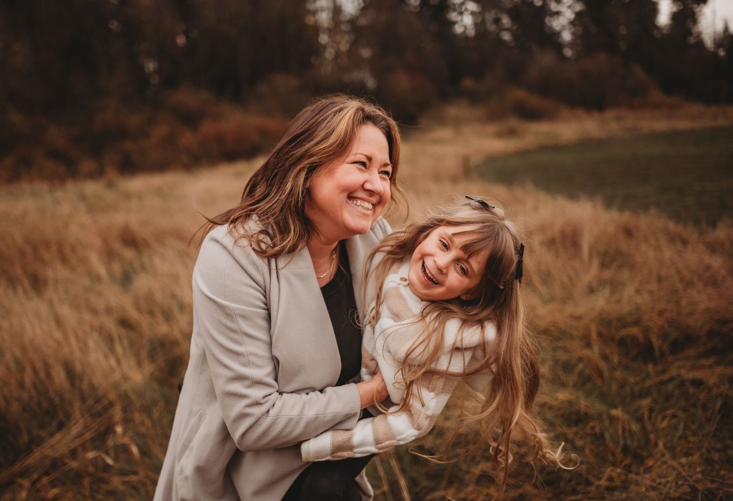 Grandmother hugging laughing young girl in autumn meadow setting.