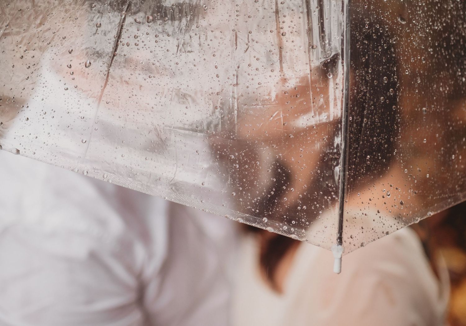 A couple shares a kiss behind a rain-dotted clear umbrella in a romantic close-up shot.