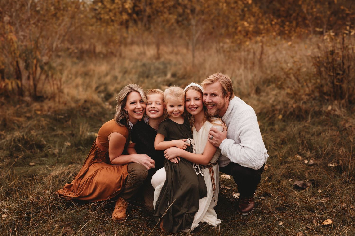 Loving family of five posing together in golden autumn field during outdoor fall photography session.