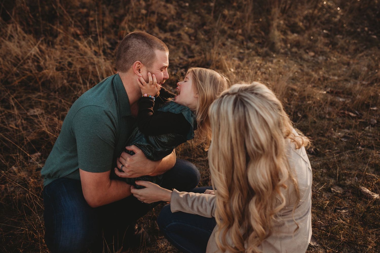 A couple leans in to kiss their child during a cozy fall family photo session outdoors.