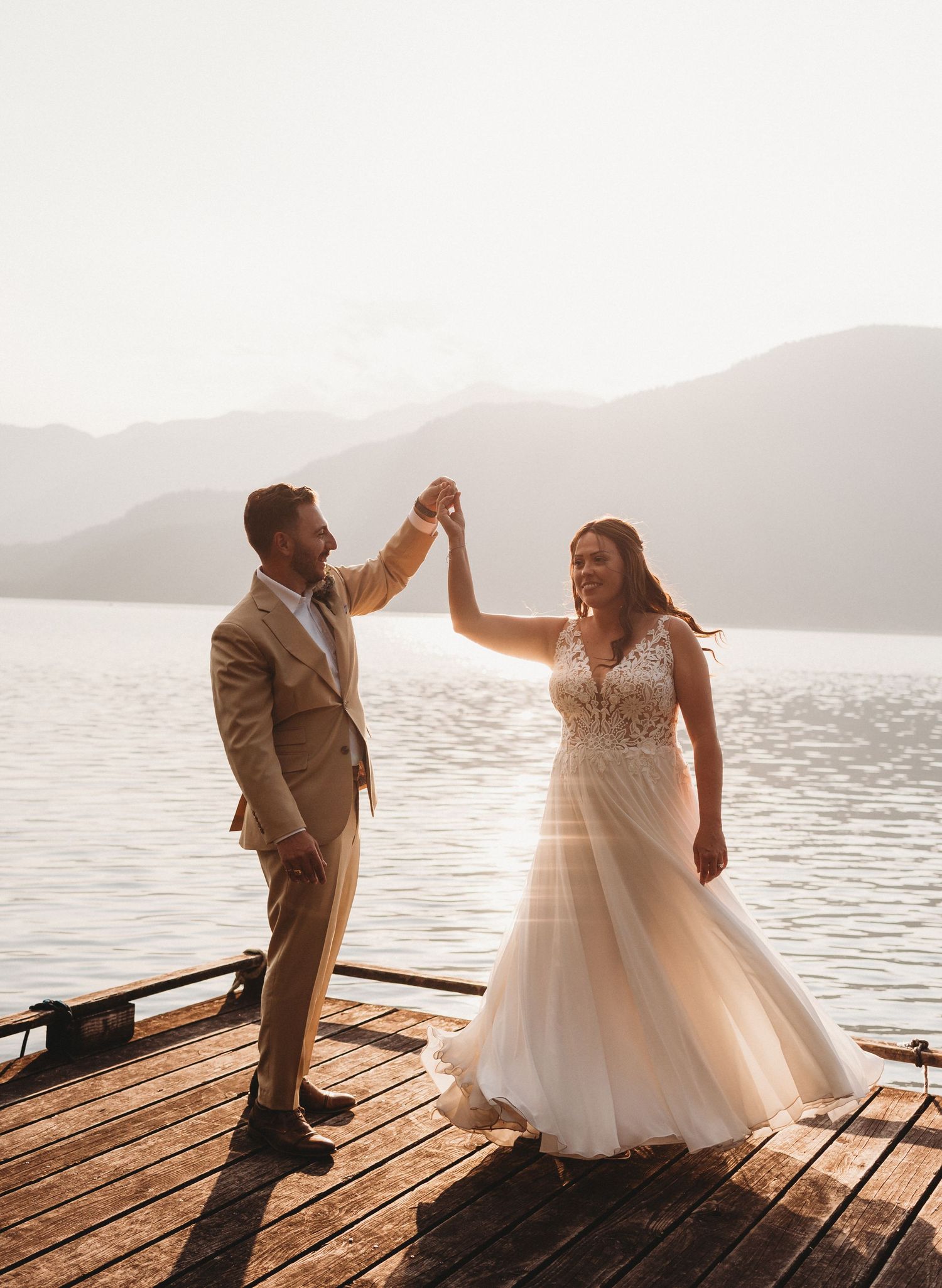 Bride and groom dance on a wooden dock with mountain lake backdrop.