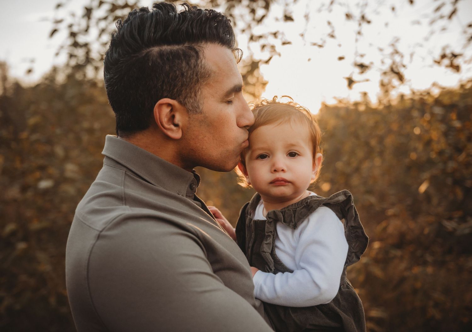 Father kissing baby on cheek in autumn golden hour.