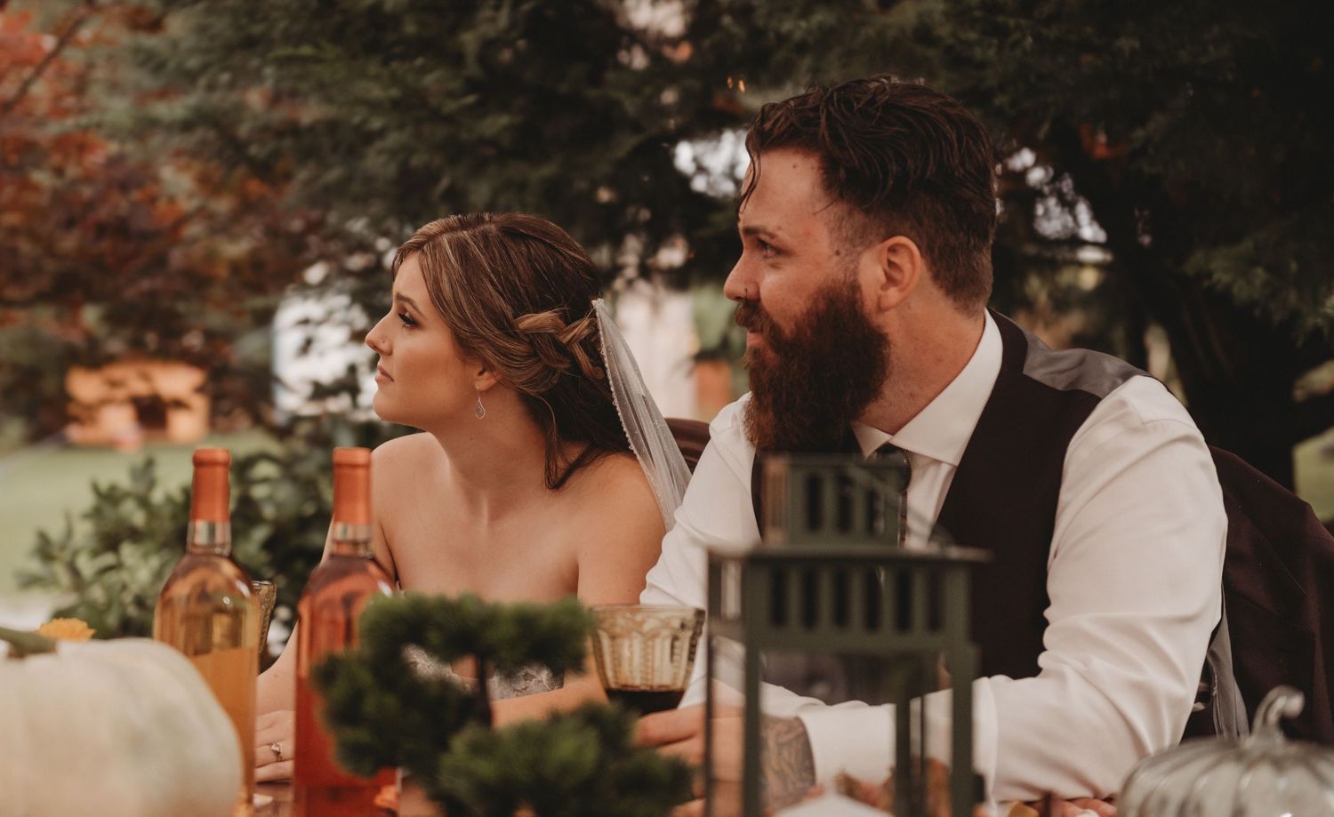 A bearded groom and bride share a romantic moment at an outdoor autumn wedding reception table.