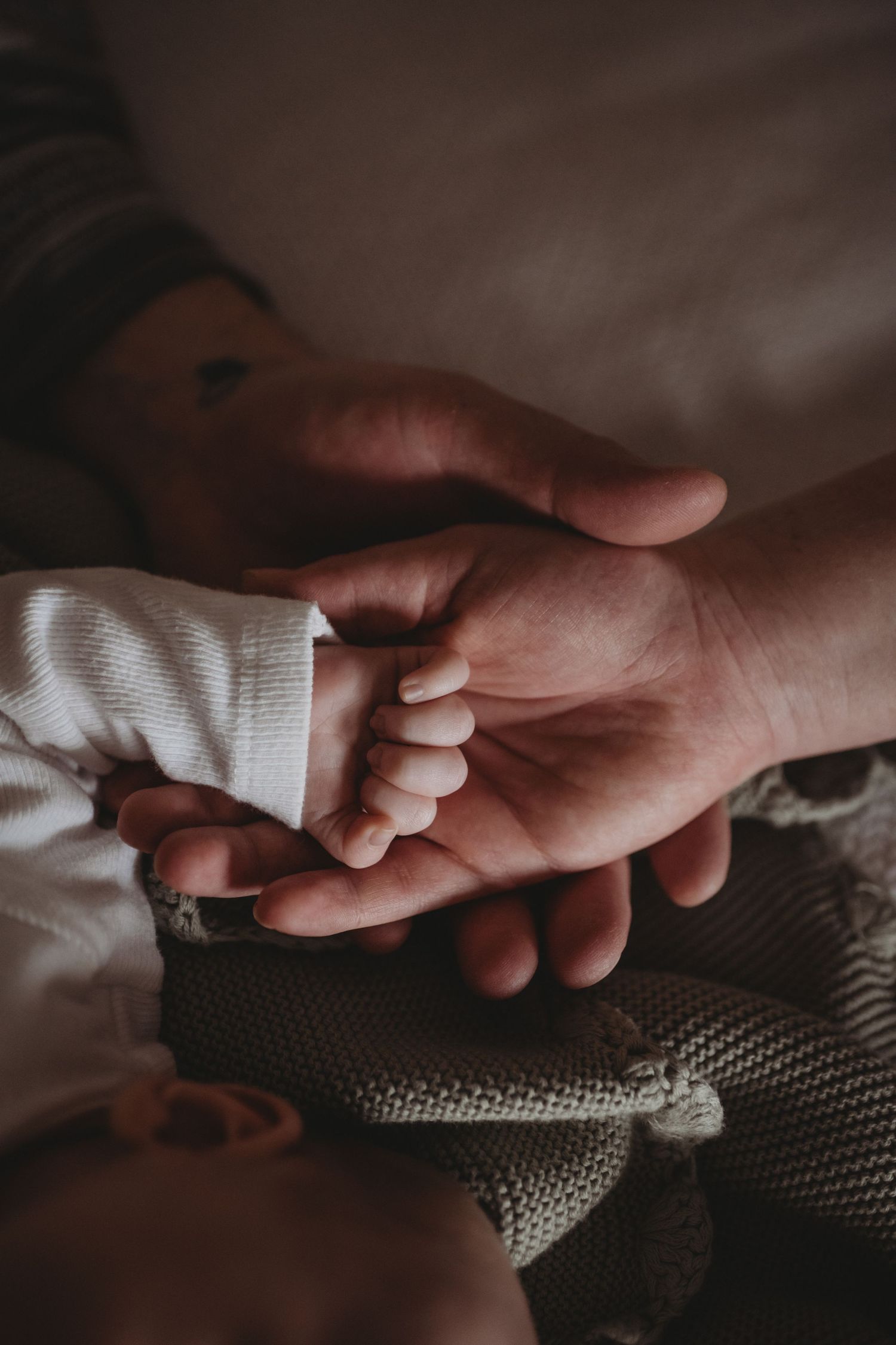 Newborn baby small hand resting in fathers open palm, tender newborn detail photography.