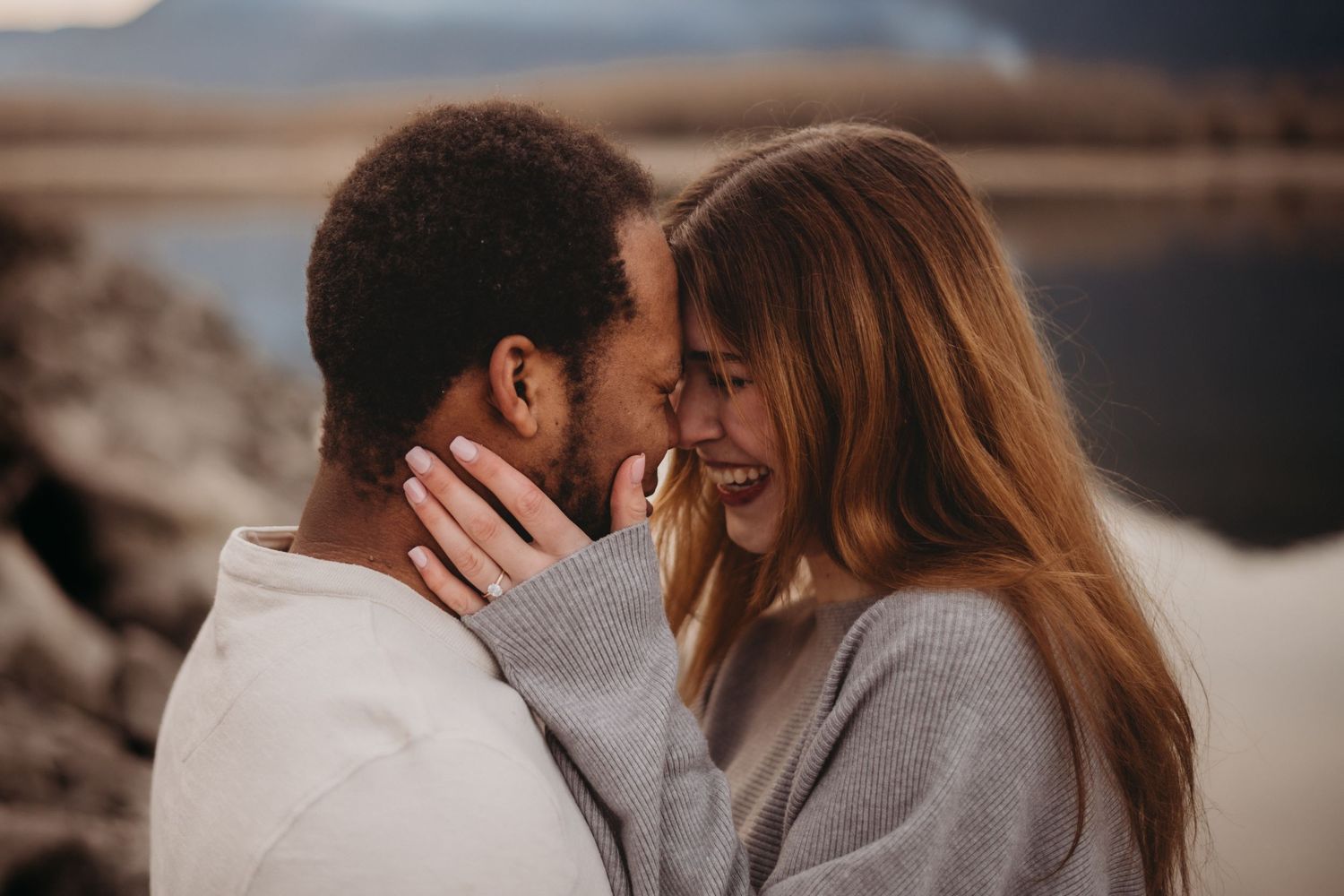 Smiling interracial couple about to kiss during romantic outdoor engagement photo session.