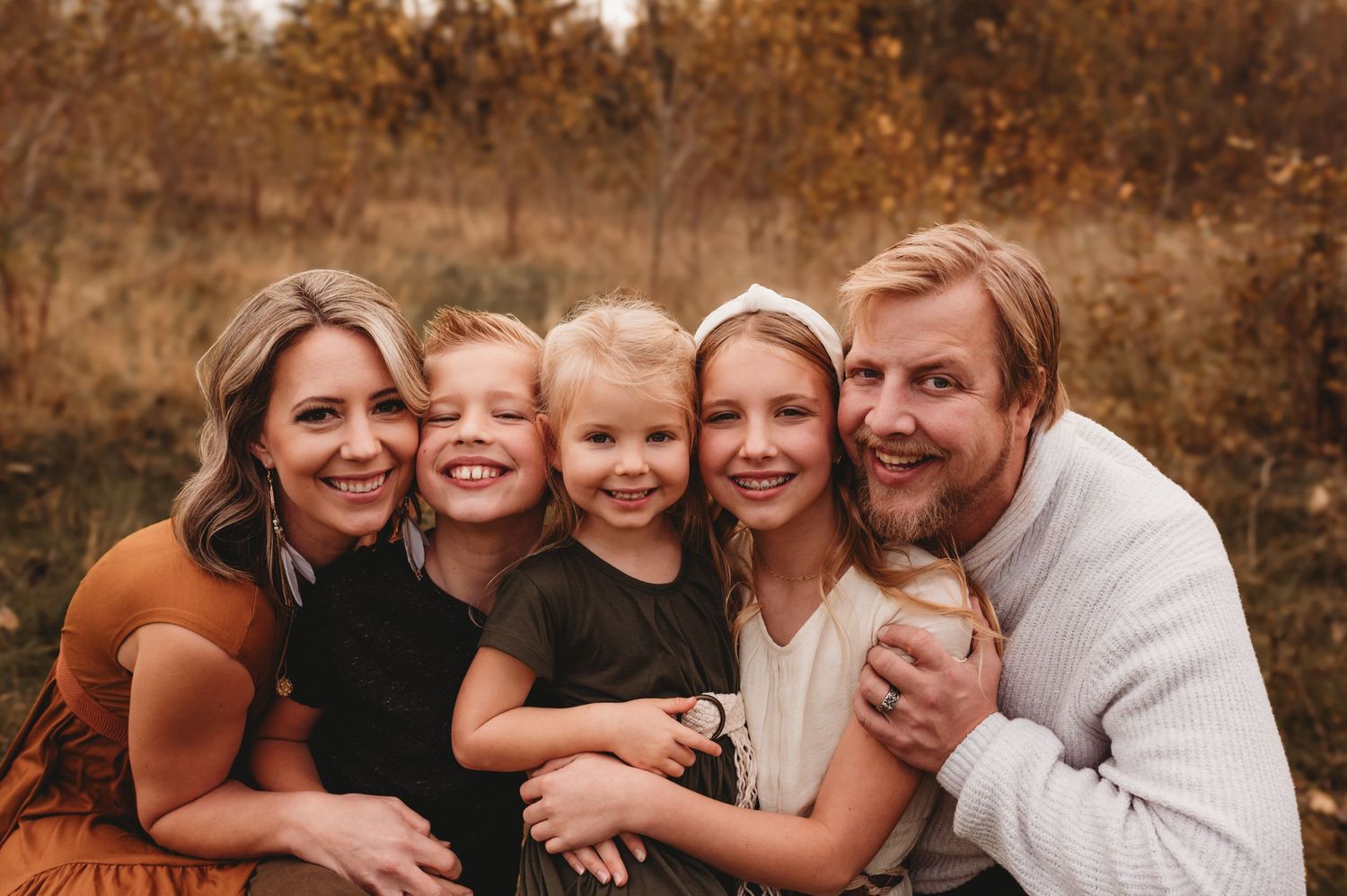Happy family of five smiling together during autumn outdoor portrait session with fall foliage background.