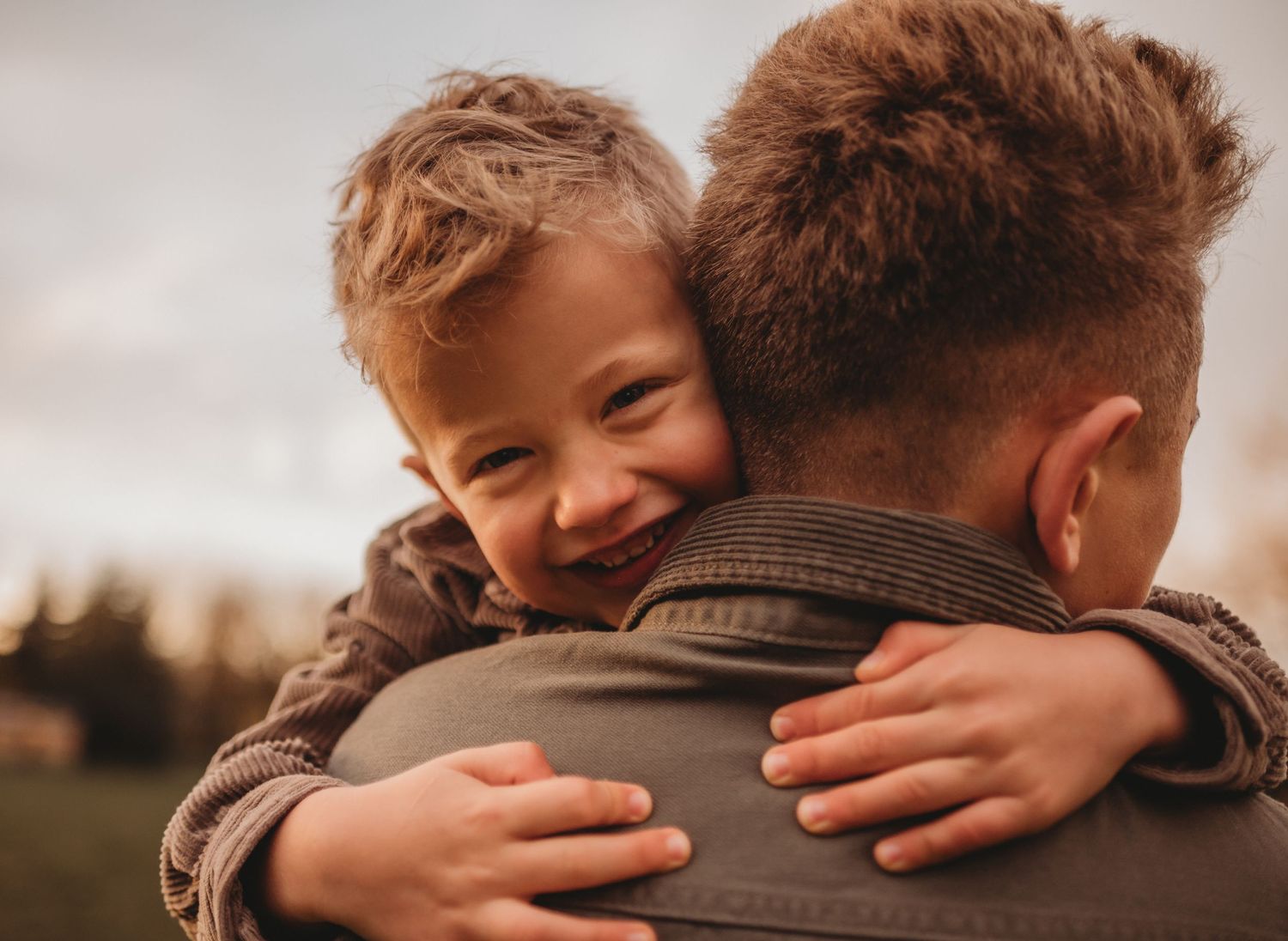A smiling toddler hugs an older boy tightly during an outdoor family photography session.