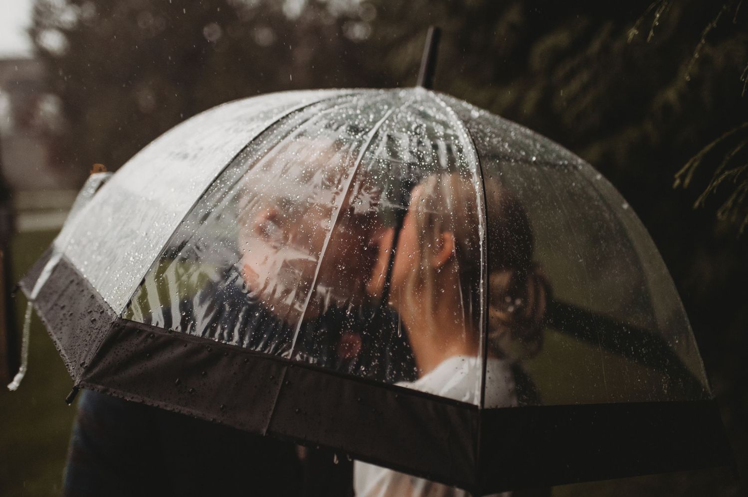 Couple sharing a romantic moment under a clear umbrella in the rain on their wedding day.