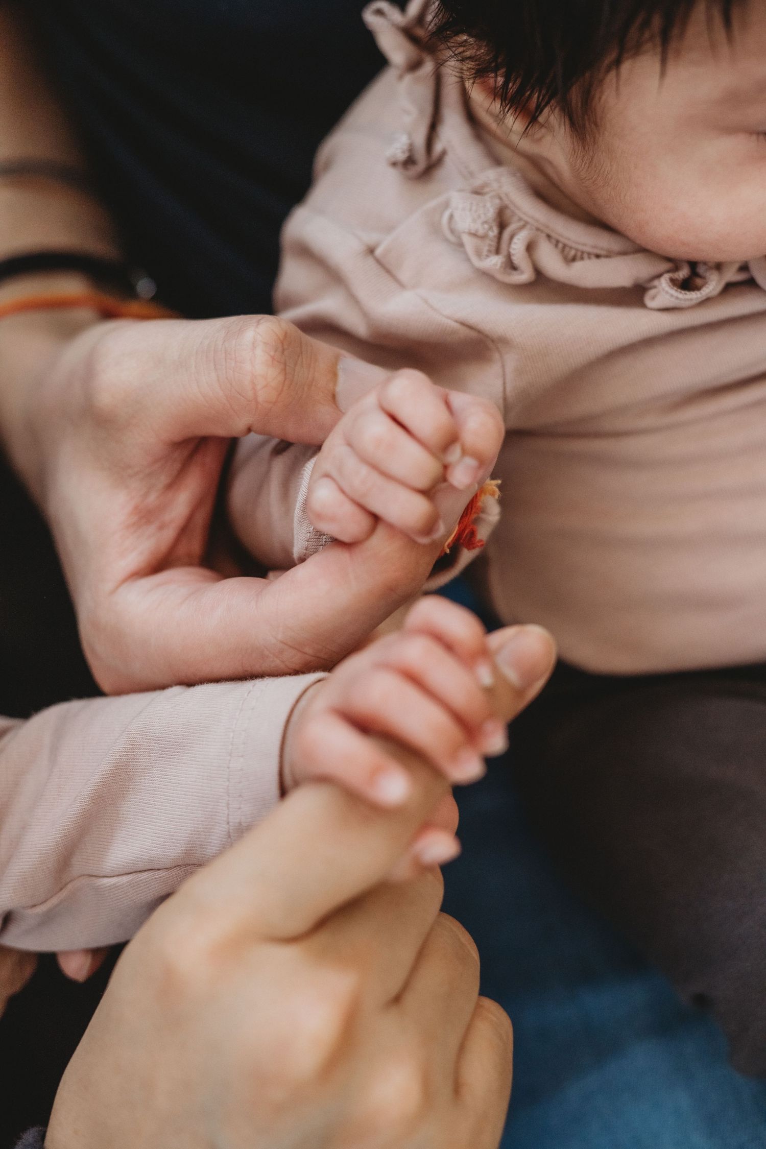 Close-up of adult hands gently holding tiny newborn baby hands in pink outfit.