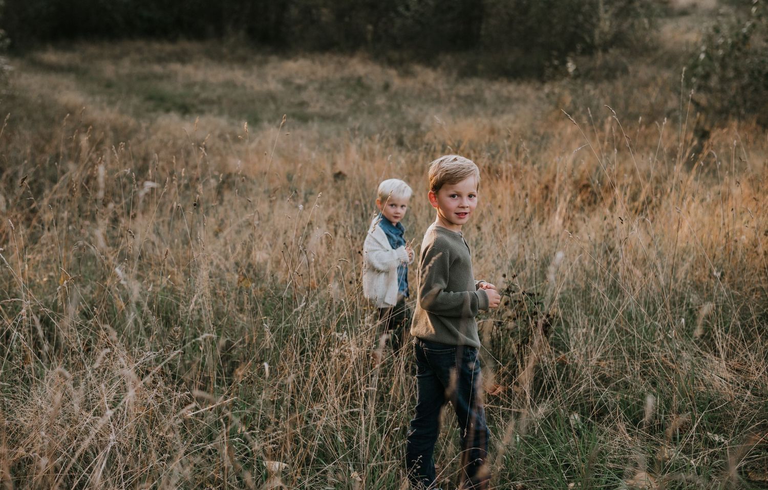 Two young boys turning to look back while standing in a dry autumn grass field.