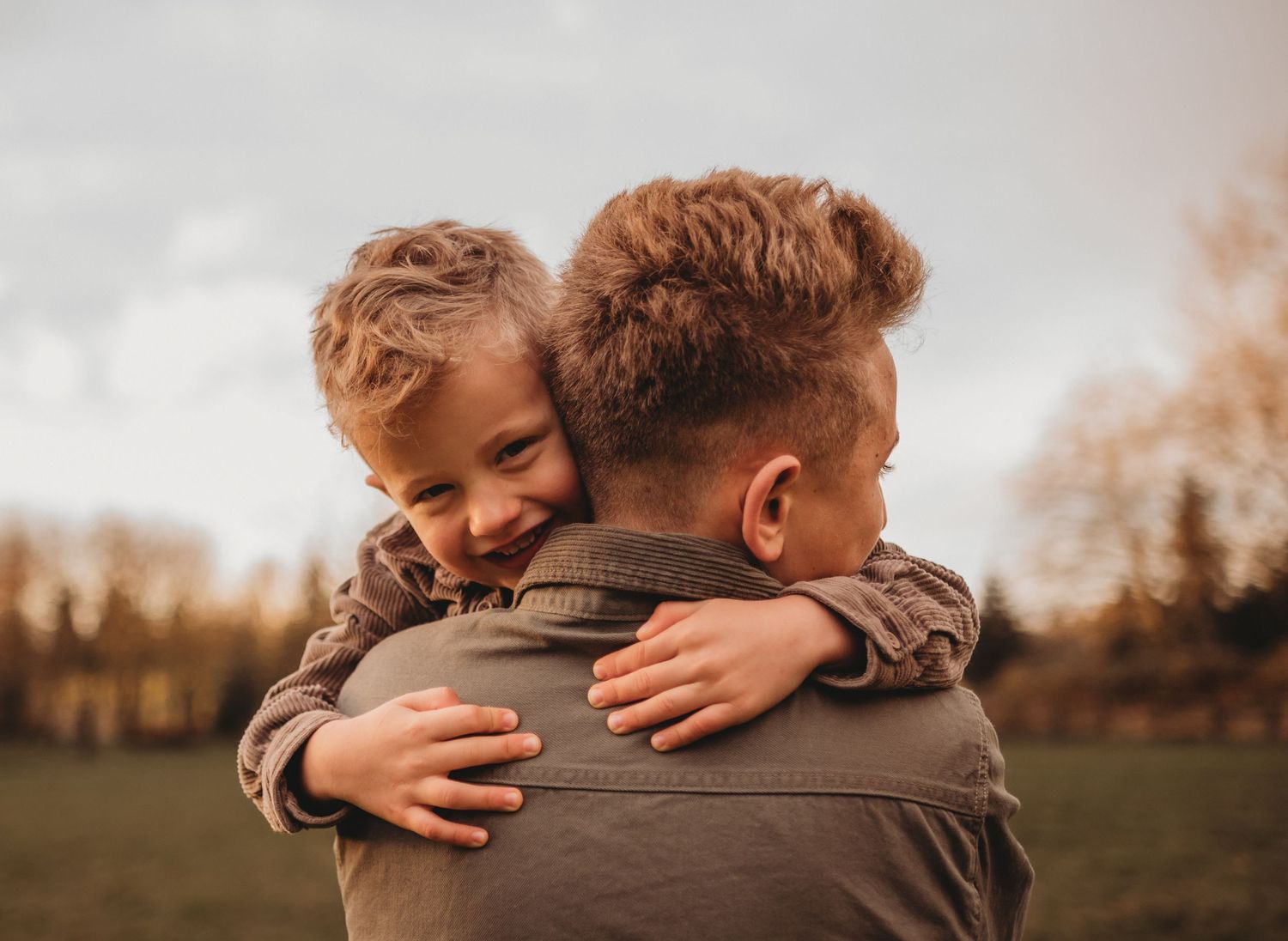 Two young brothers share a warm hug outdoors during a golden autumn family photo session.