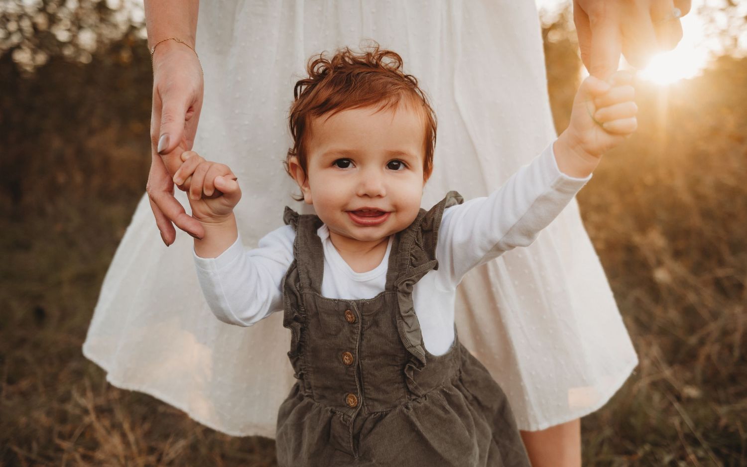 Cheerful toddler girl raising arms in golden autumn light.