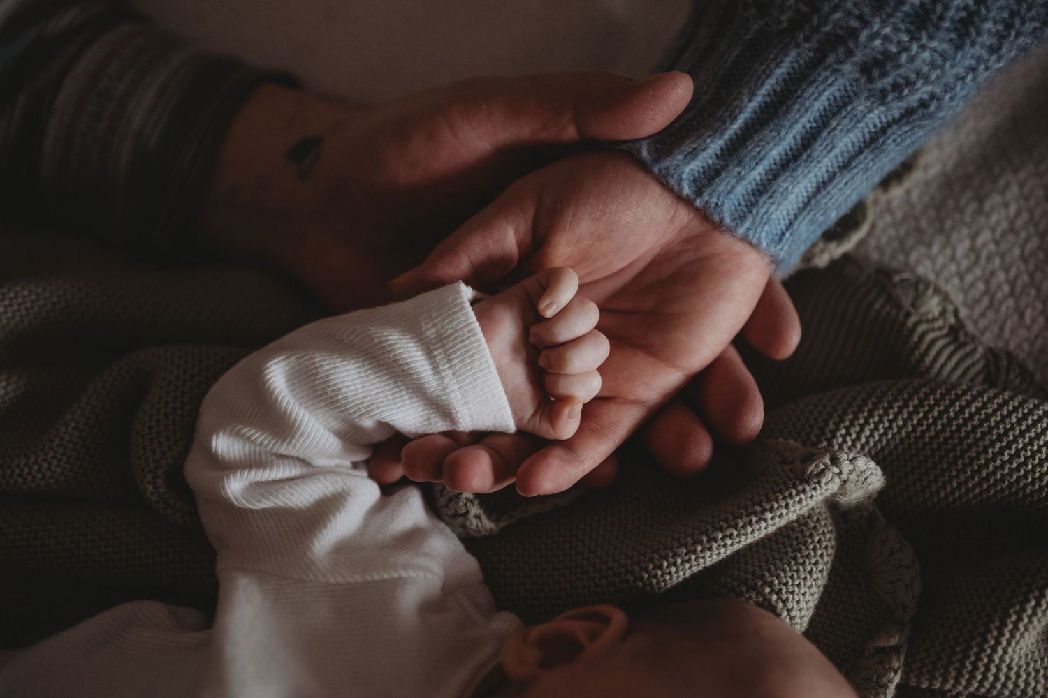 Newborn baby tiny hand resting in parent's palm, close-up newborn detail photography.