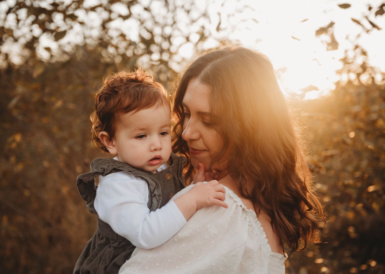 Mother holding baby in glowing autumn sunset outdoors.