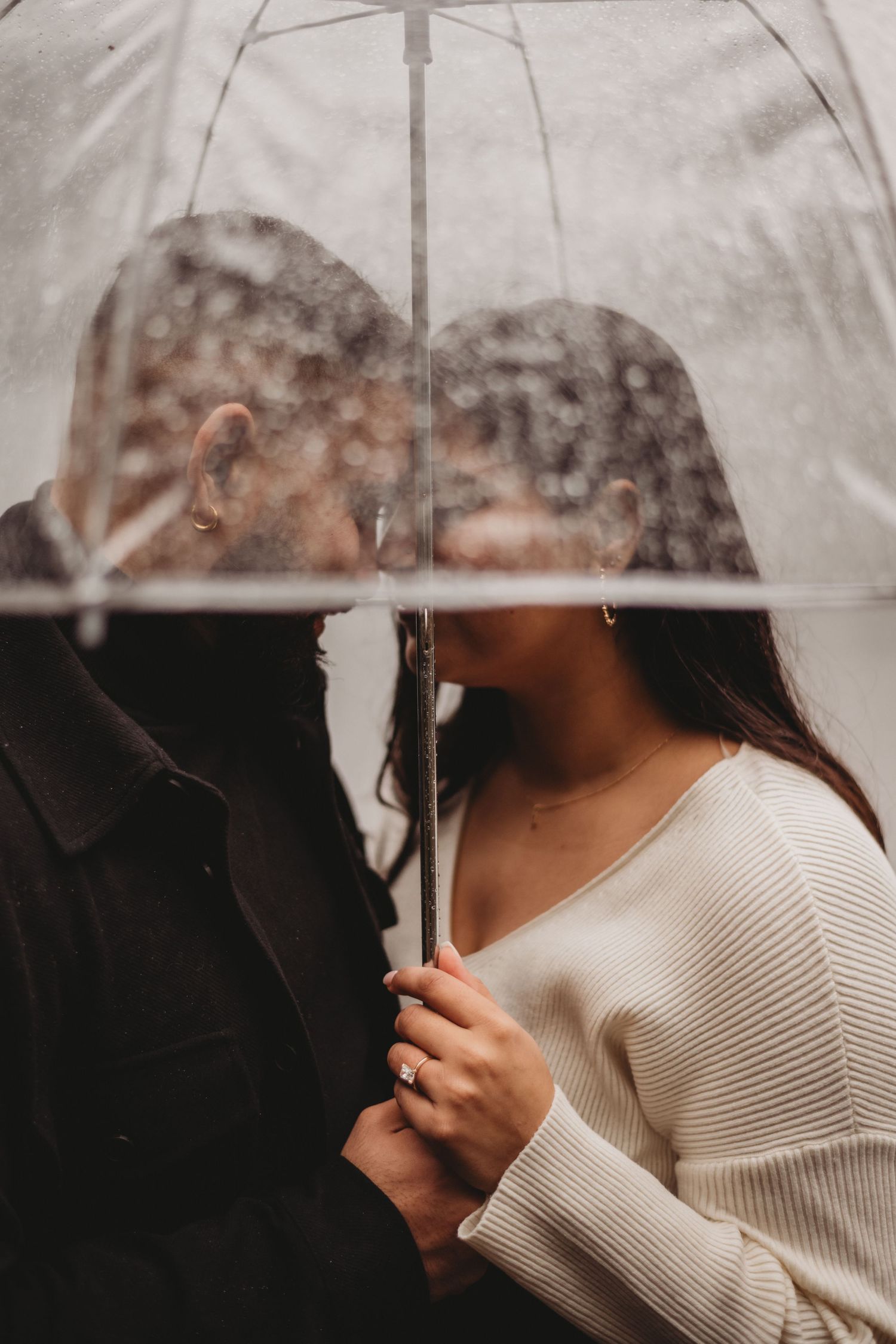 Romantic couple sharing an intimate moment under a clear umbrella in the rain.