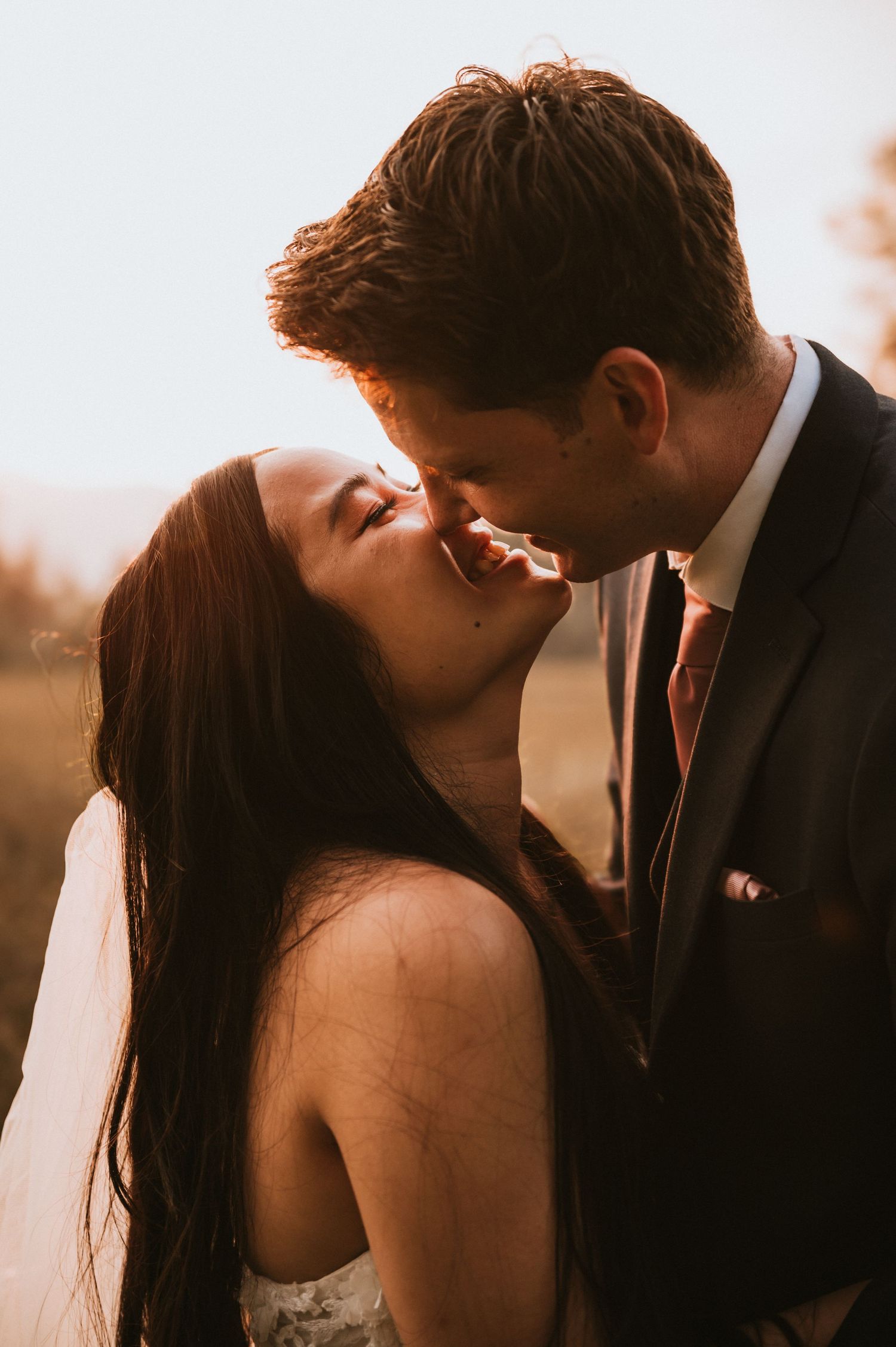 Close-up of bride and groom sharing a kiss in warm golden sunset light outdoors.