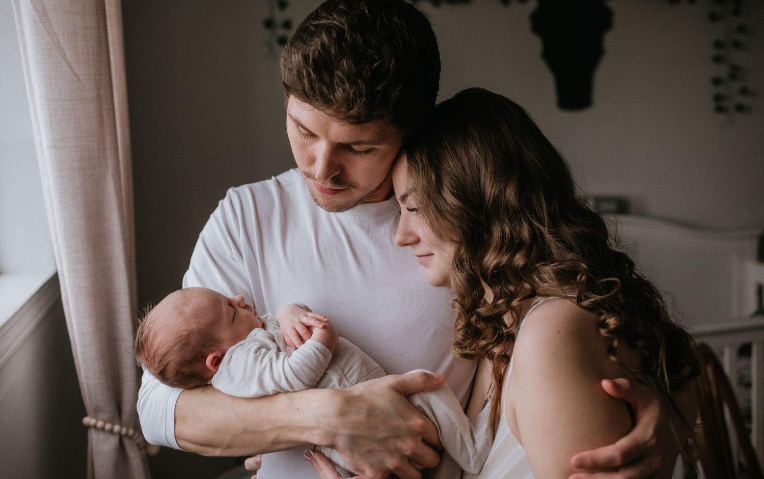 Young couple sharing tender moment together holding newborn baby in warmly lit bedroom.