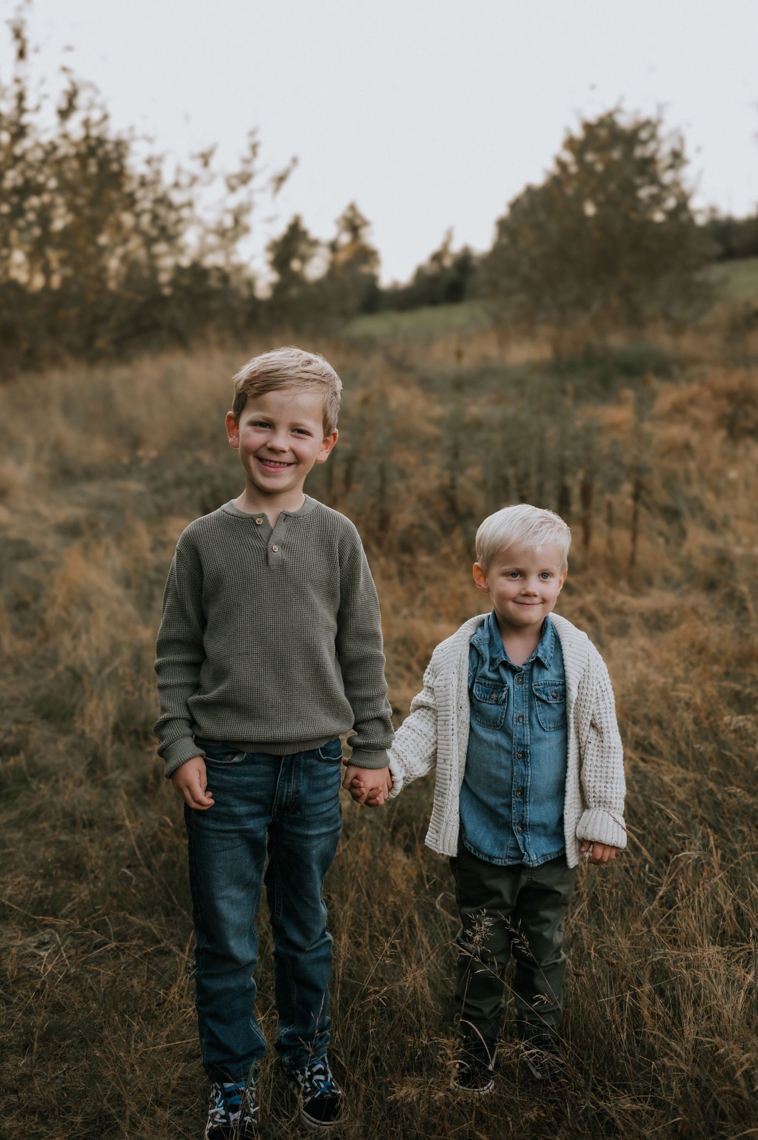 Two young brothers holding hands and smiling in a golden autumn field at sunset.