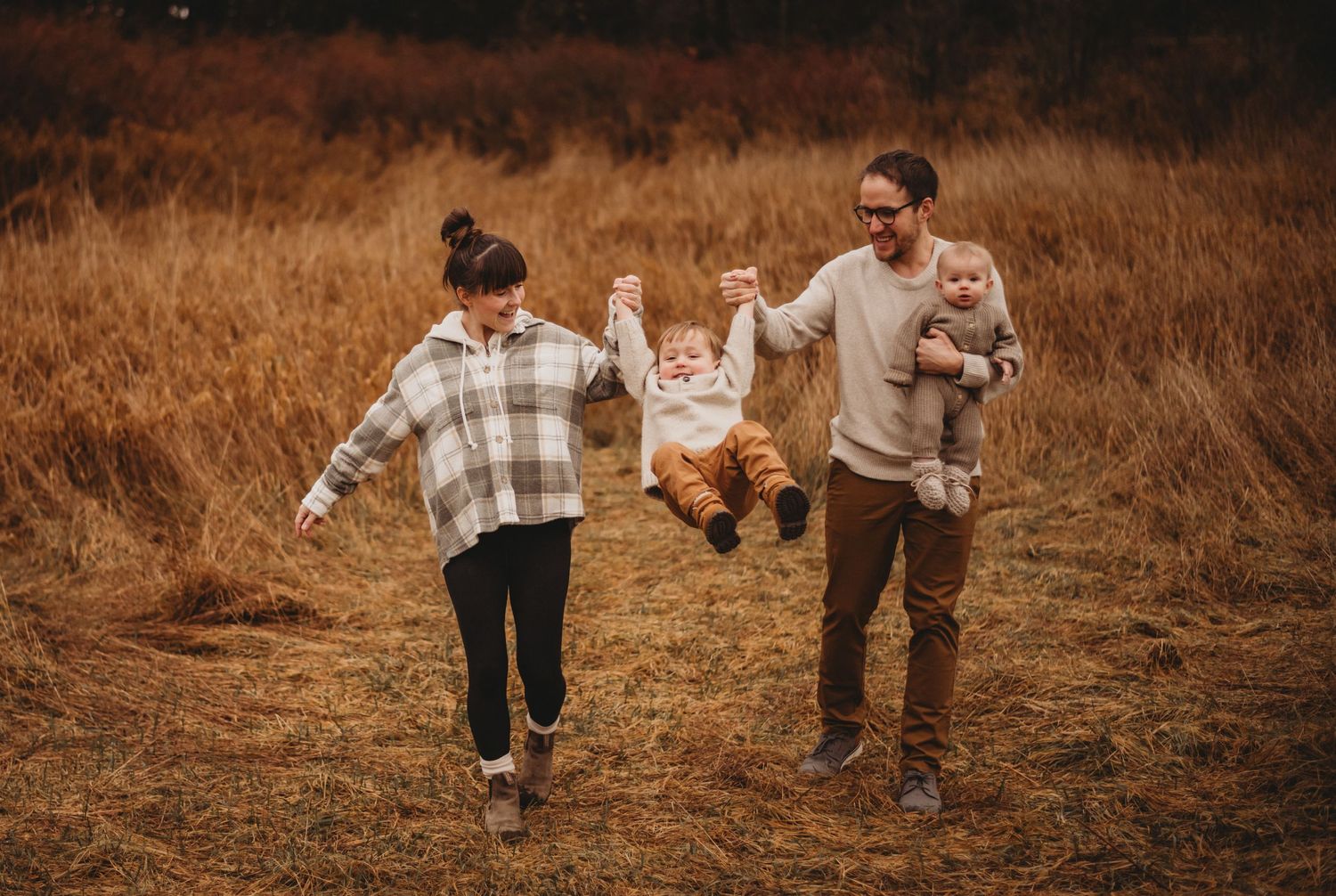 Happy family swinging toddler between parents walking in golden autumn field.