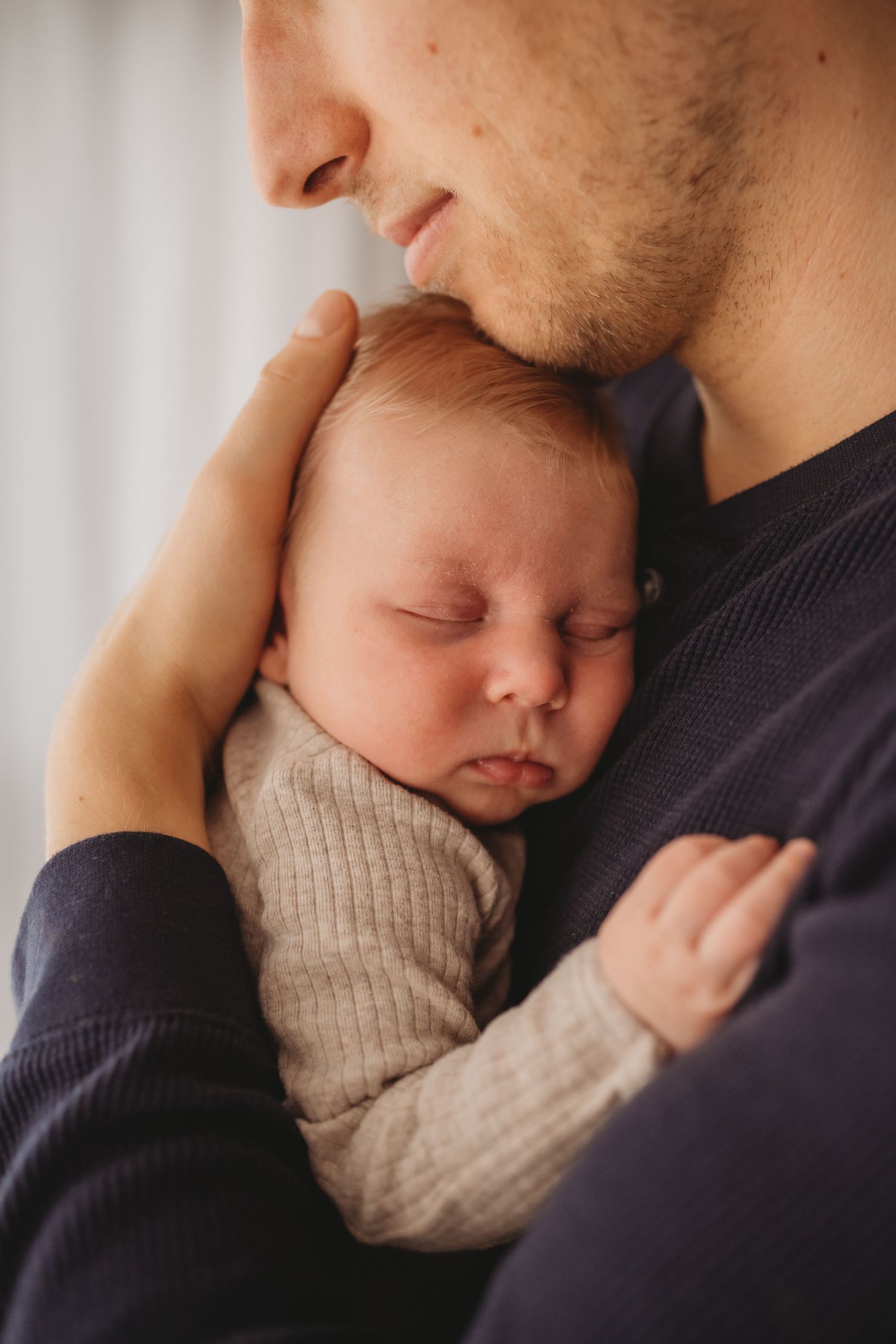 Close-up of father cradling sleeping newborn baby against his chest in soft gray outfit.