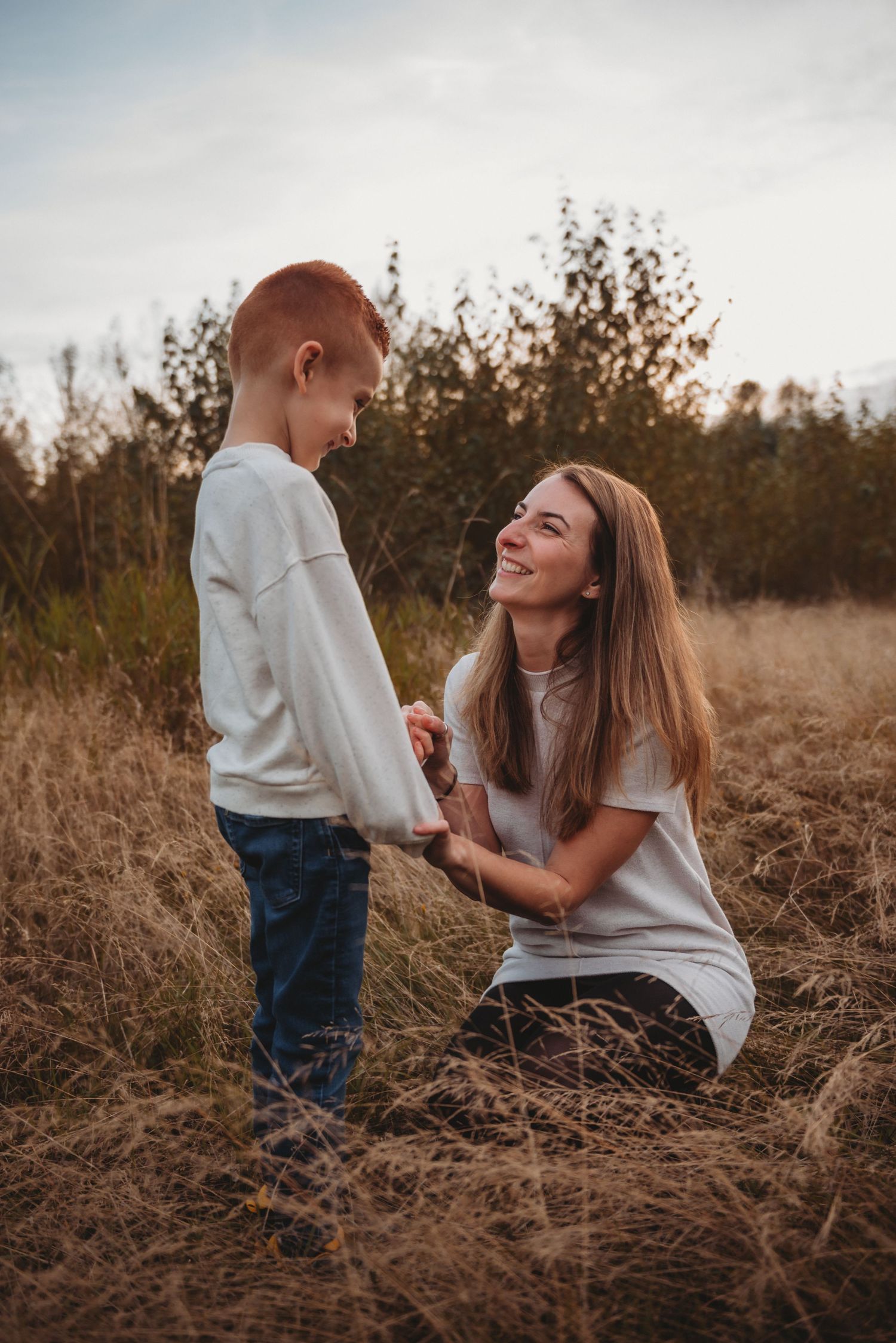 Smiling mother kneeling in golden field holding hands with her young red-haired son.