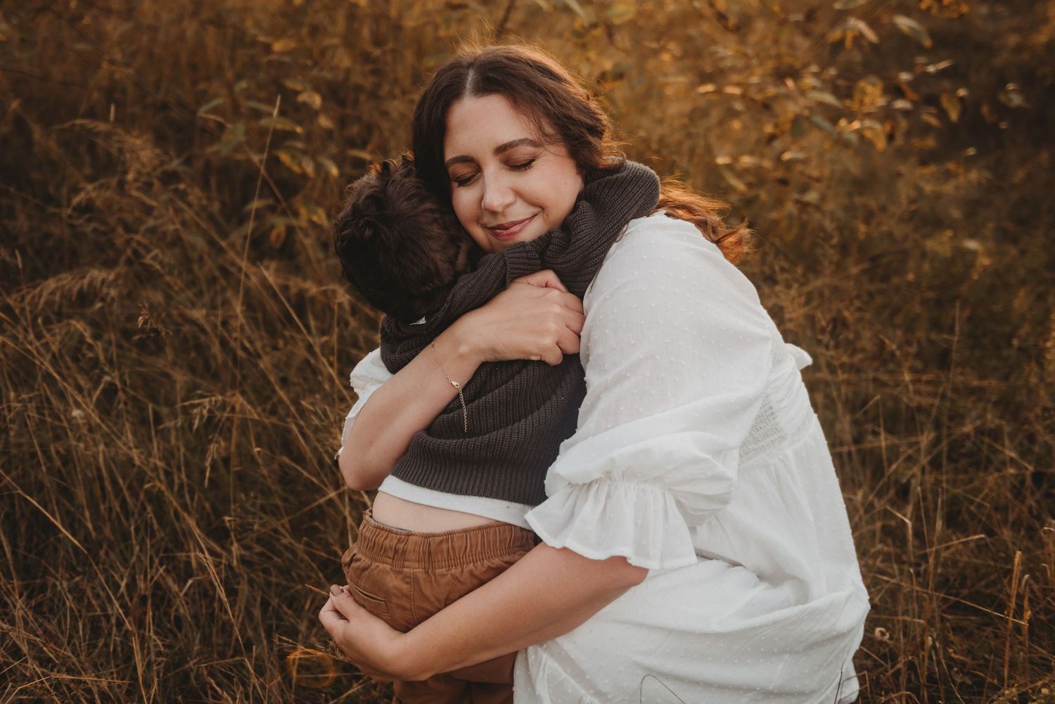 Mother and young son sharing a warm embrace in a golden autumn field at sunset.