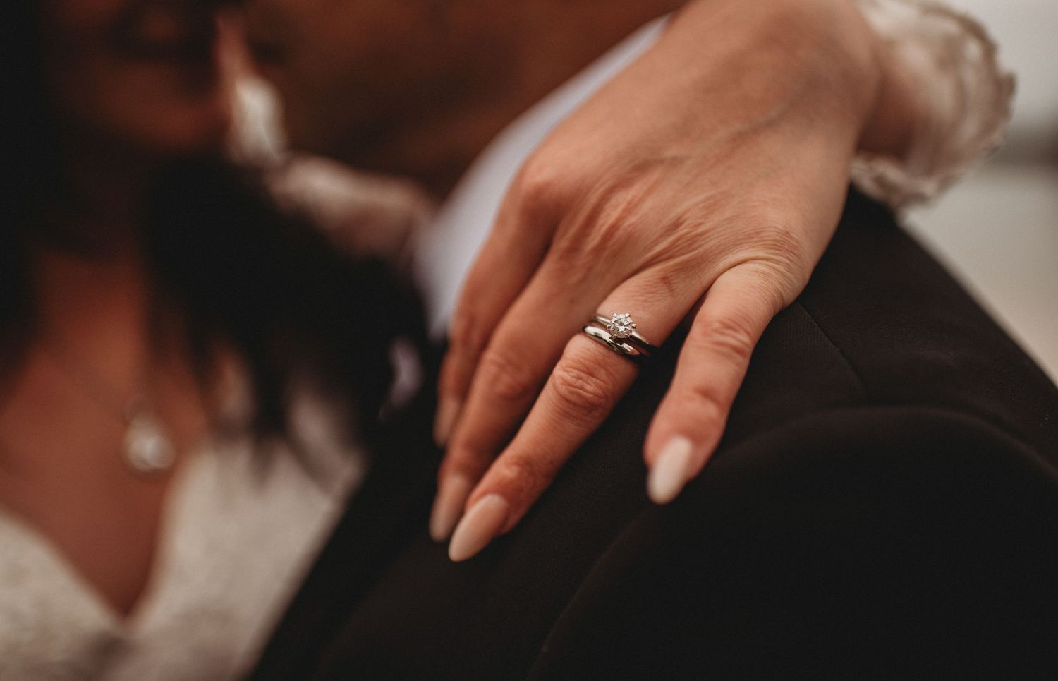 Close-up of a bride's hand resting on groom's suit, showcasing a sparkling diamond engagement ring.