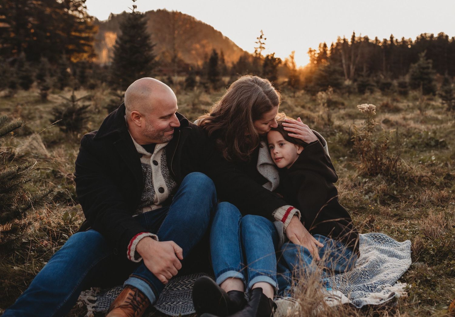 A loving family sits together on a blanket in a golden meadow enjoying a warm sunset moment.