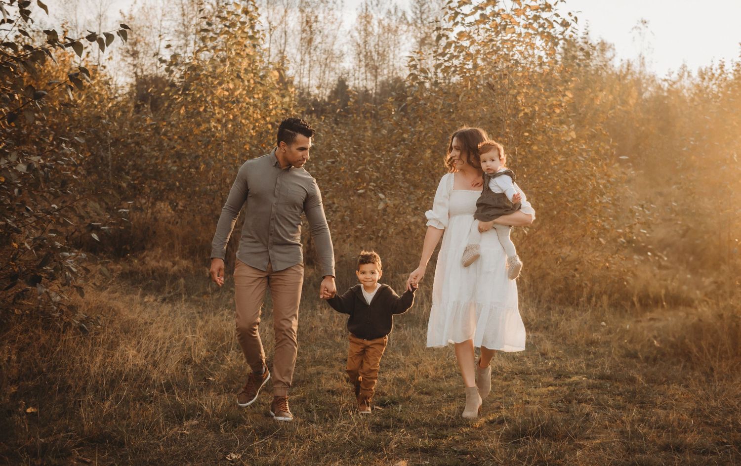 A family of four strolls through a sun-drenched autumn field during a warm outdoor session.
