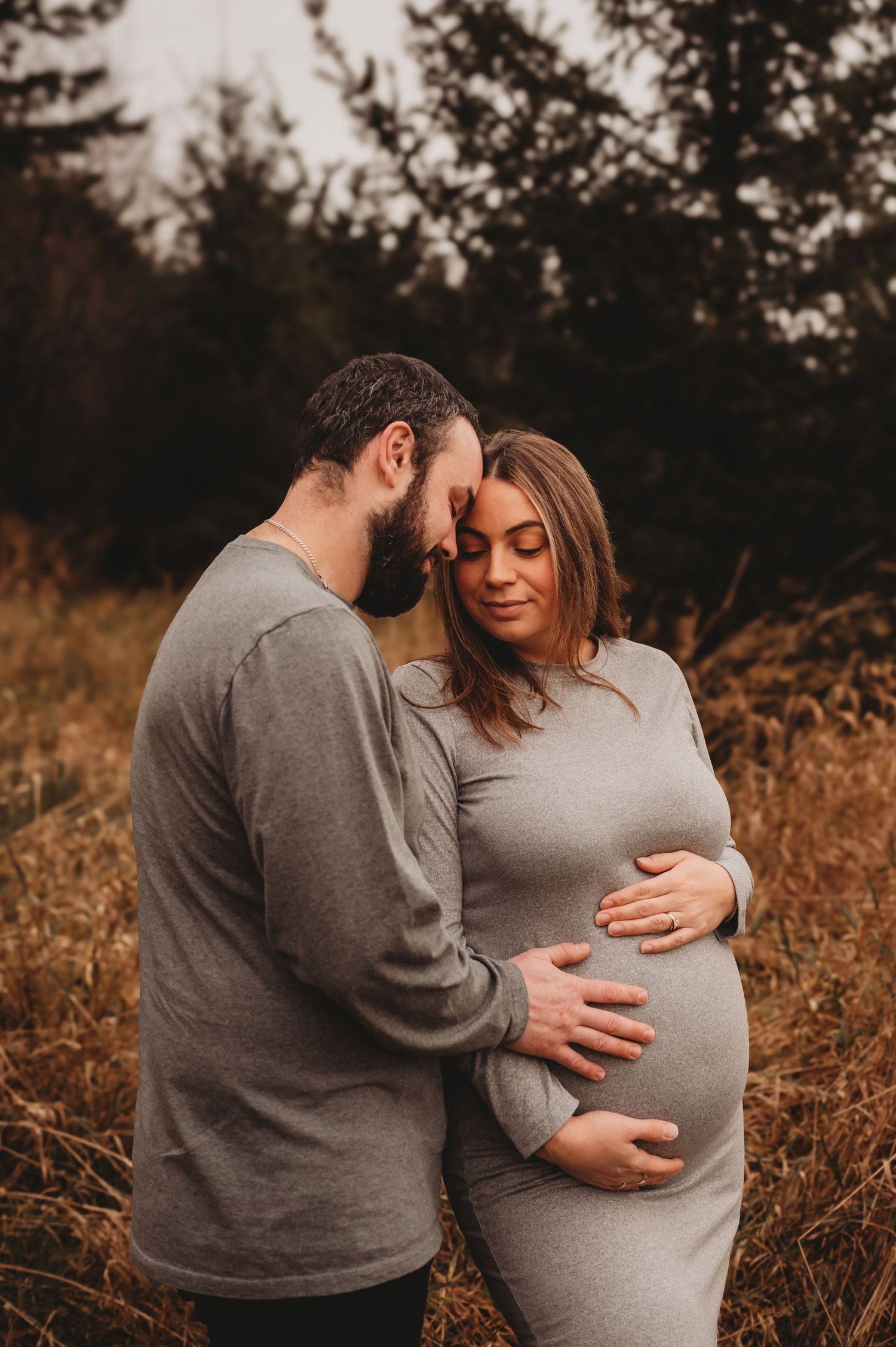 Couple tenderly embracing in autumn field, hands on pregnant belly.