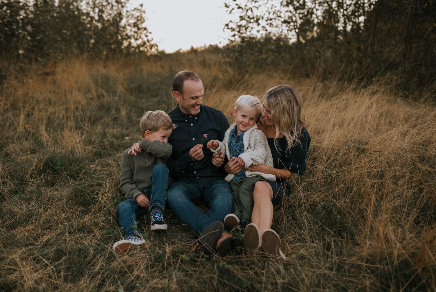 Happy family of four sitting together in a golden autumn field laughing and playing.