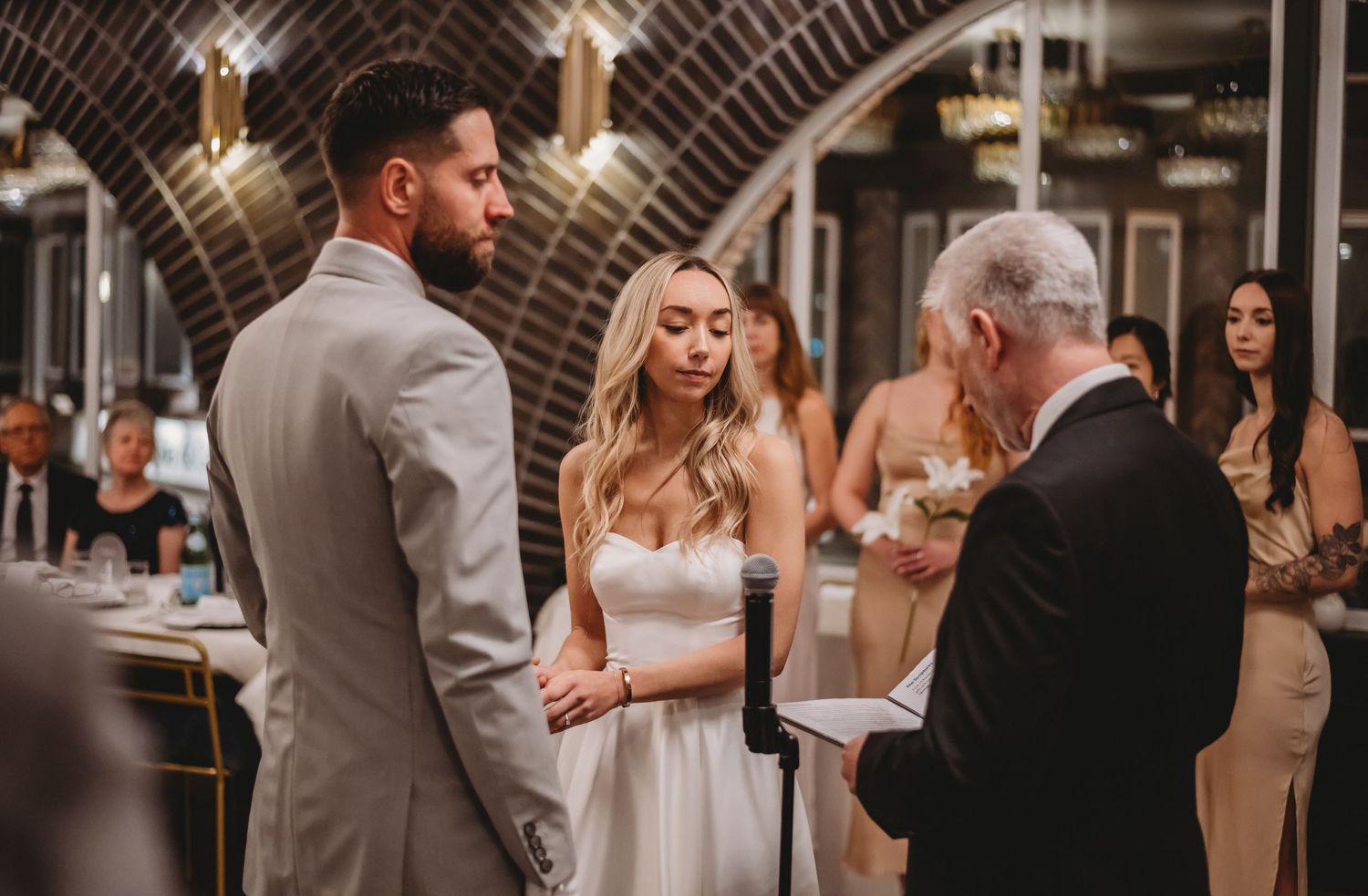 Bride and groom exchange vows during an intimate indoor wedding ceremony with guests.