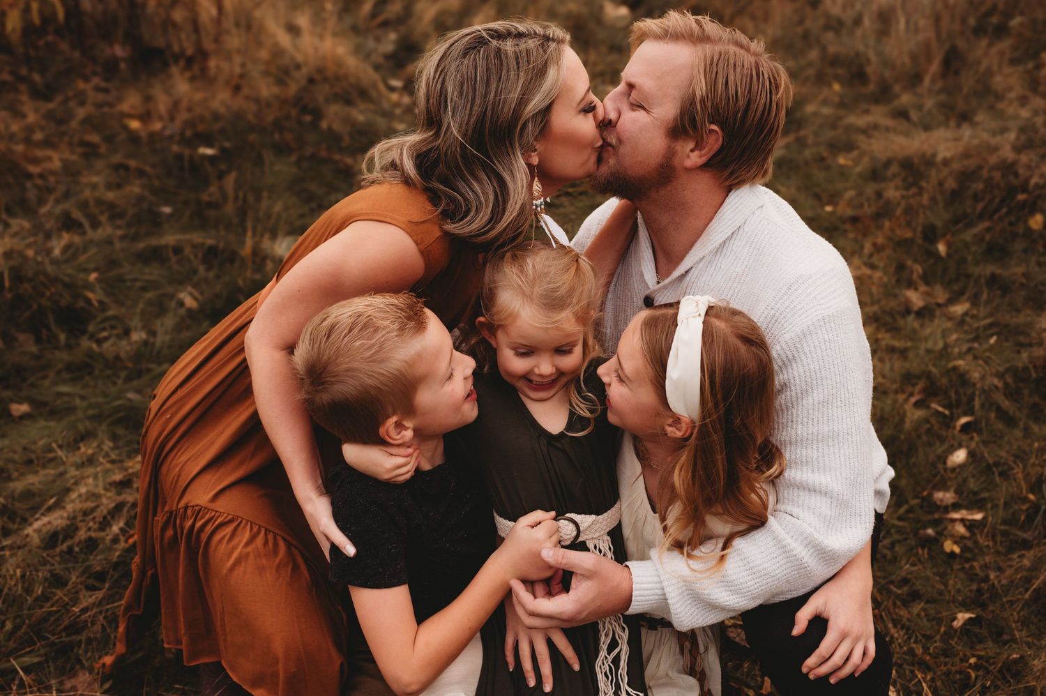 Happy family of five sharing kisses and hugs in golden autumn field portrait.